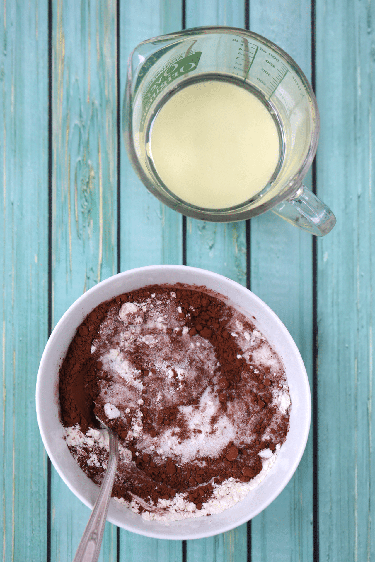 Ingredients for 2-Minute Microwave Brownie Bowl are separately prepared. Dry ingredients in a bowl including cocoa powder, all-purpose flour, sugar, and slat. Wet ingredients in a liquid measuring jug including milk, oil, and vanilla extract. 