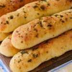 Garlic Breadsticks are shaped into long, thin rods and were baked until golden brown. The exterior looks slightly crispy with brushed butter, garlic and herbs.