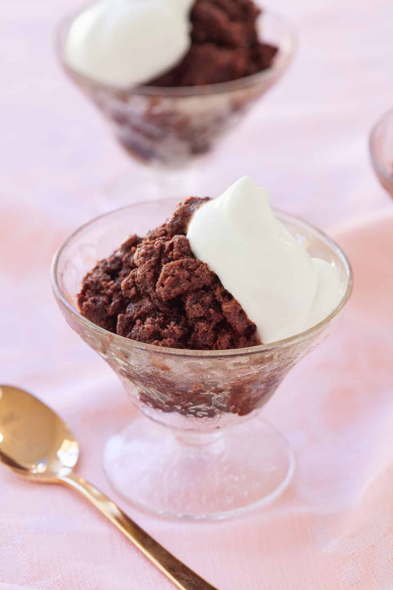 Perfectly crunchy decadent chocolate granita is served in clear textured glass dessert cups with light softly whipped fresh cream on top. A golden spoon is in the bottom left corner. 