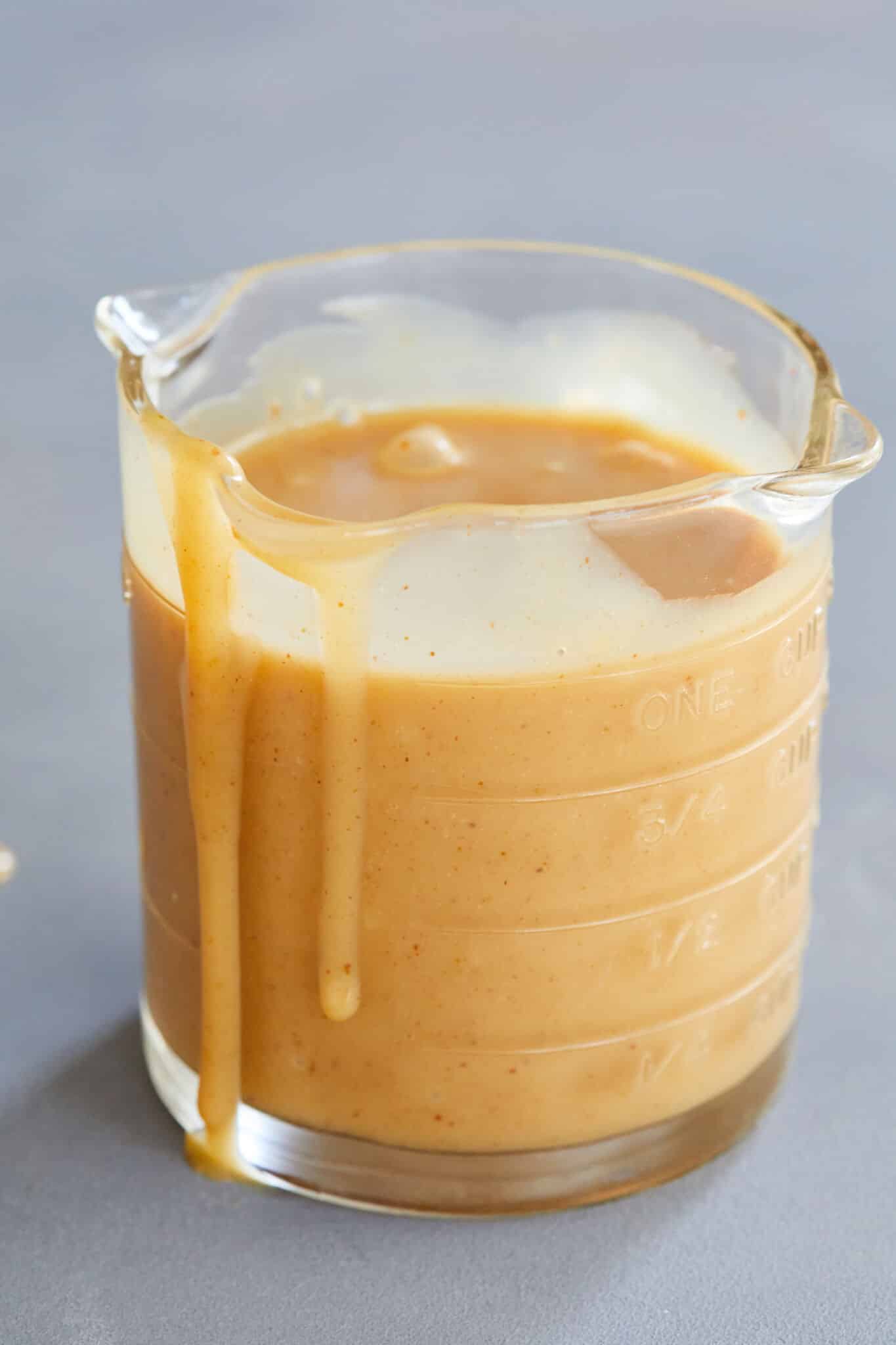 The thick and creamy peanut butter ice cream sauce is stored in a 3-spout glass measuring jug, with a little dripping down on the side. 