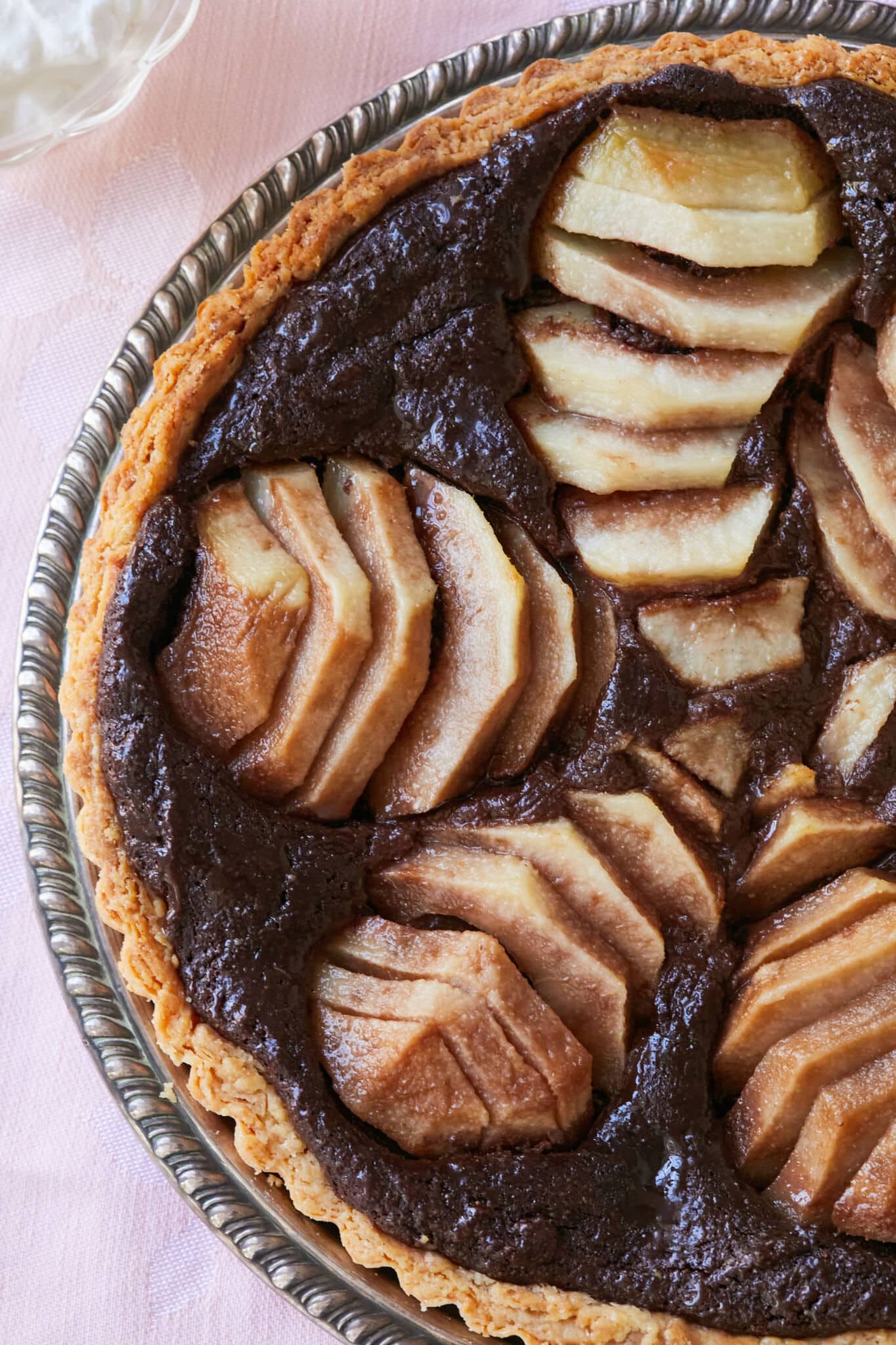 A decadent Pear and Chocolate Frangipane Tart is served on a silver platter. It has golden crispy crust, a lush almond cocoa filling topped with meltingly tender sliced pears. 