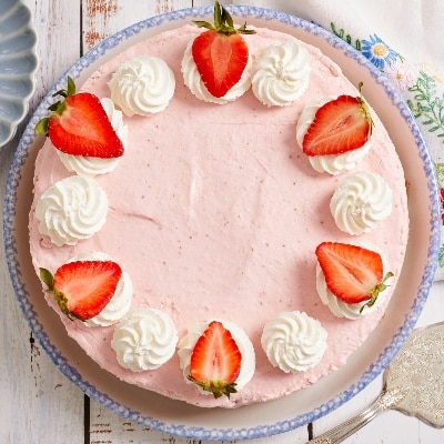 Pink Strawberry Cheesecake is topped with whipped cream and strawberry halves.