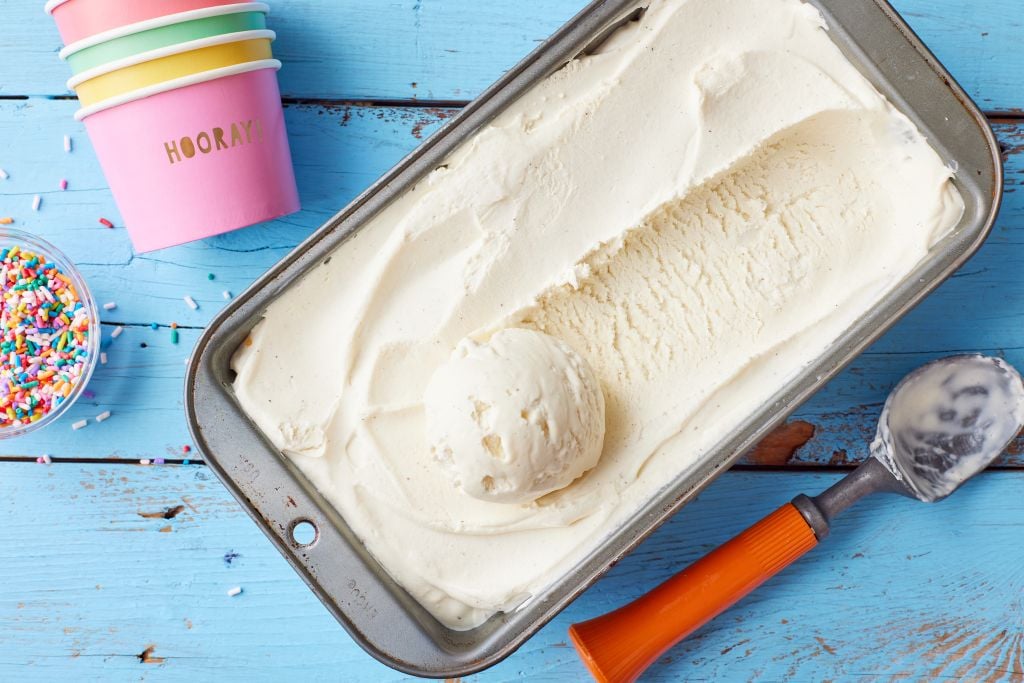 A top-down view of a loaf tin of vanilla ice cream with paper cups and a scoop on the side