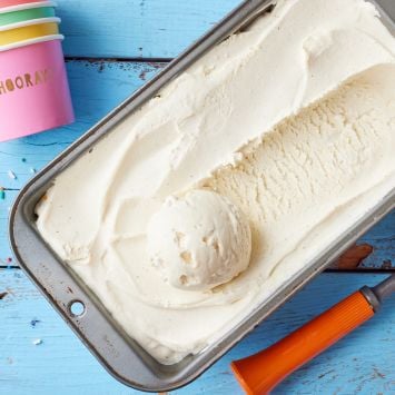 A top-down view of a loaf tin of vanilla ice cream with paper cups and a scoop on the side