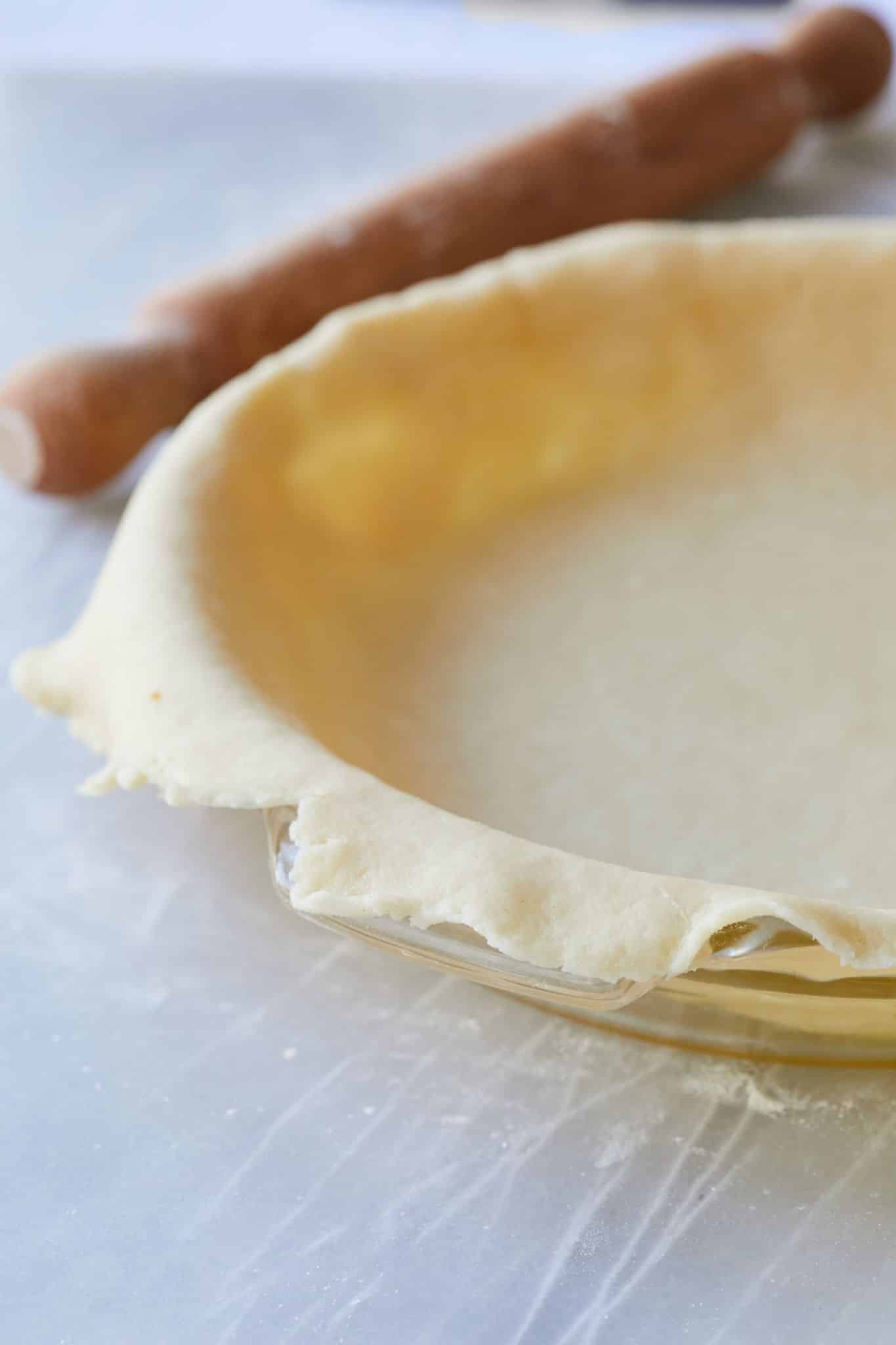 A glass pie dish is lined with sour cream pie crust, with the rolling next to it. 