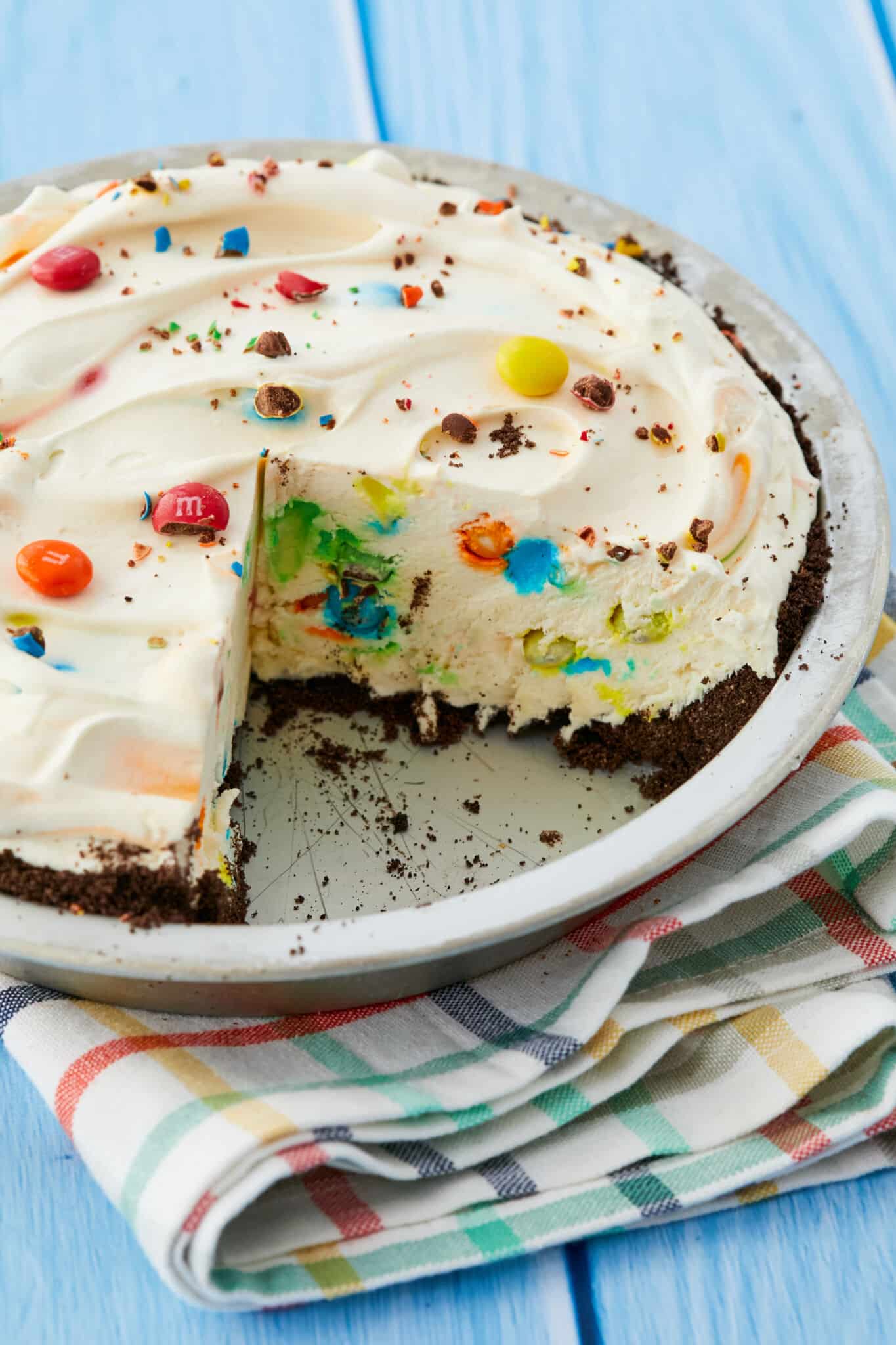 A thick ice cream pie in a metal pan, with Oreo cookie crust, silky white ice cream and colorful M&Ms mixed through out. 