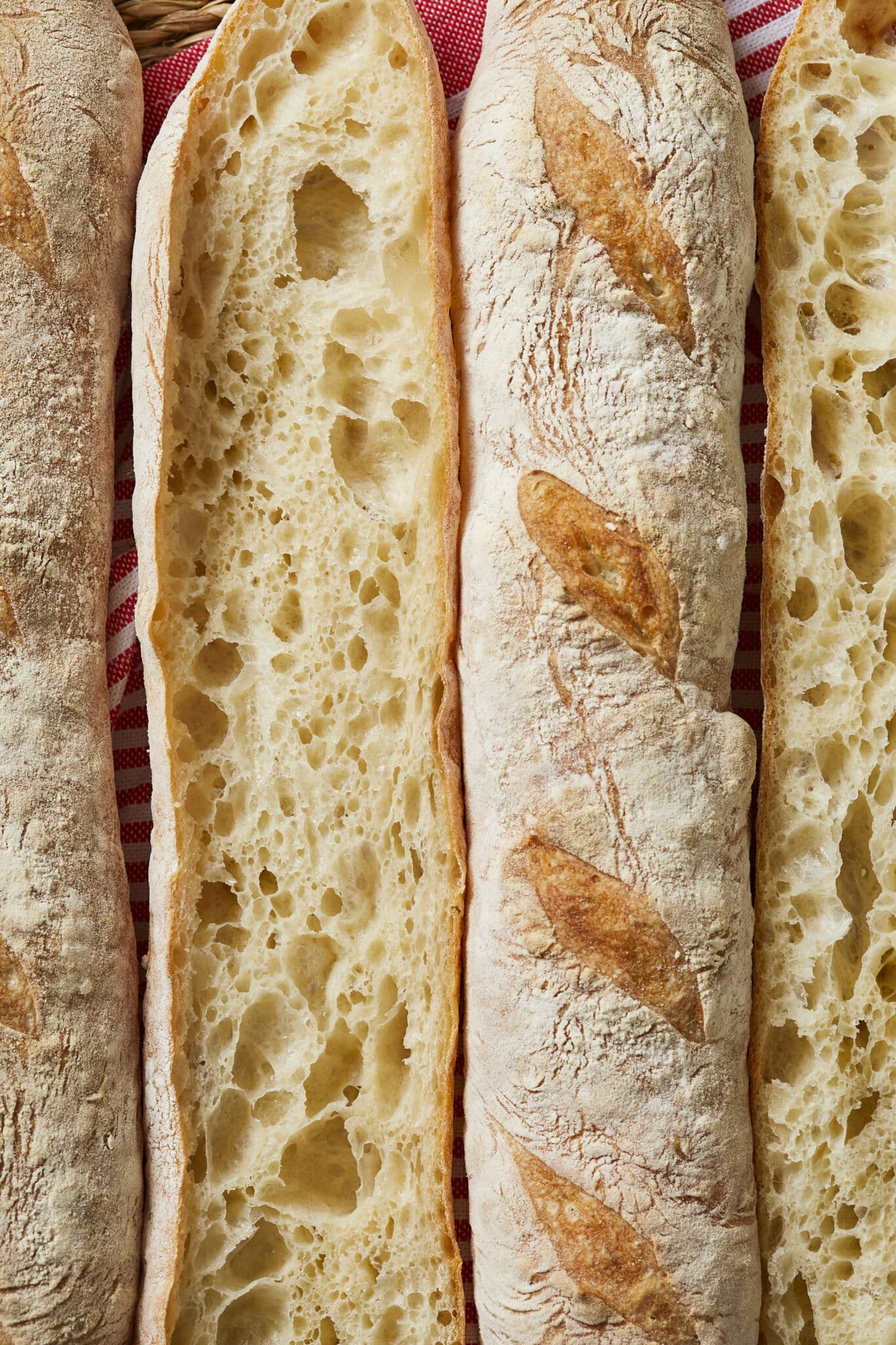 The Easiest No Knead Baguettes were cut open, with two showing the crispy golden brown crust and the other two showing the lacy crumb with deep air pockets. 