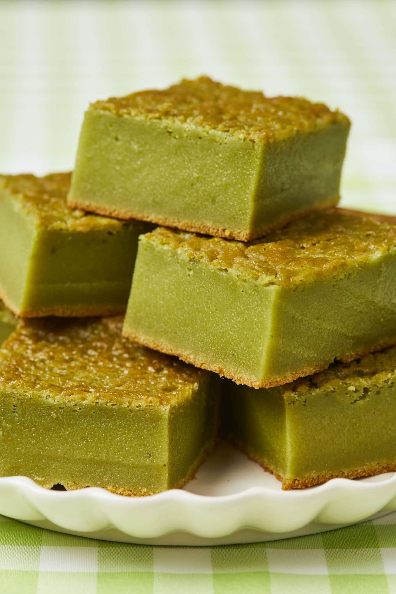 A close shot of 5 green Matcha Butter Mochi on a white plate with crispy golden crust on top and fine chewy crumb.