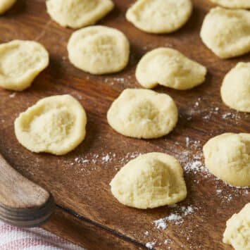 Freshly made Orecchiette Pasta is drying on a floured wooden board. This unique semolina pasta is small, round, and slightly domed with an indented center, resembling tears and making it great for capturing the various toppings and condiments.