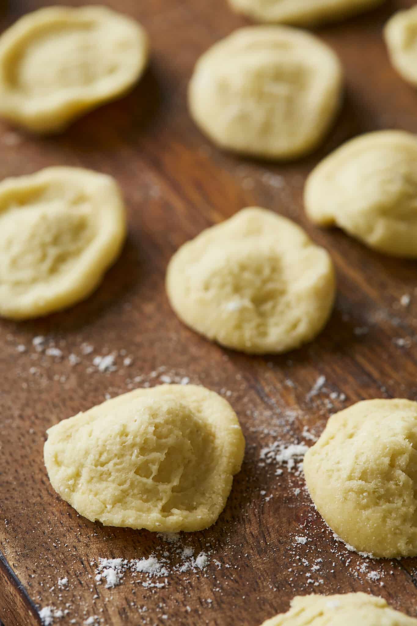 Freshly made Orecchiette Pasta is drying on a floured wooden board. This unique semolina pasta is small, round, and slightly domed with an indented center, resembling tears and making it great for capturing the various toppings and condiments.