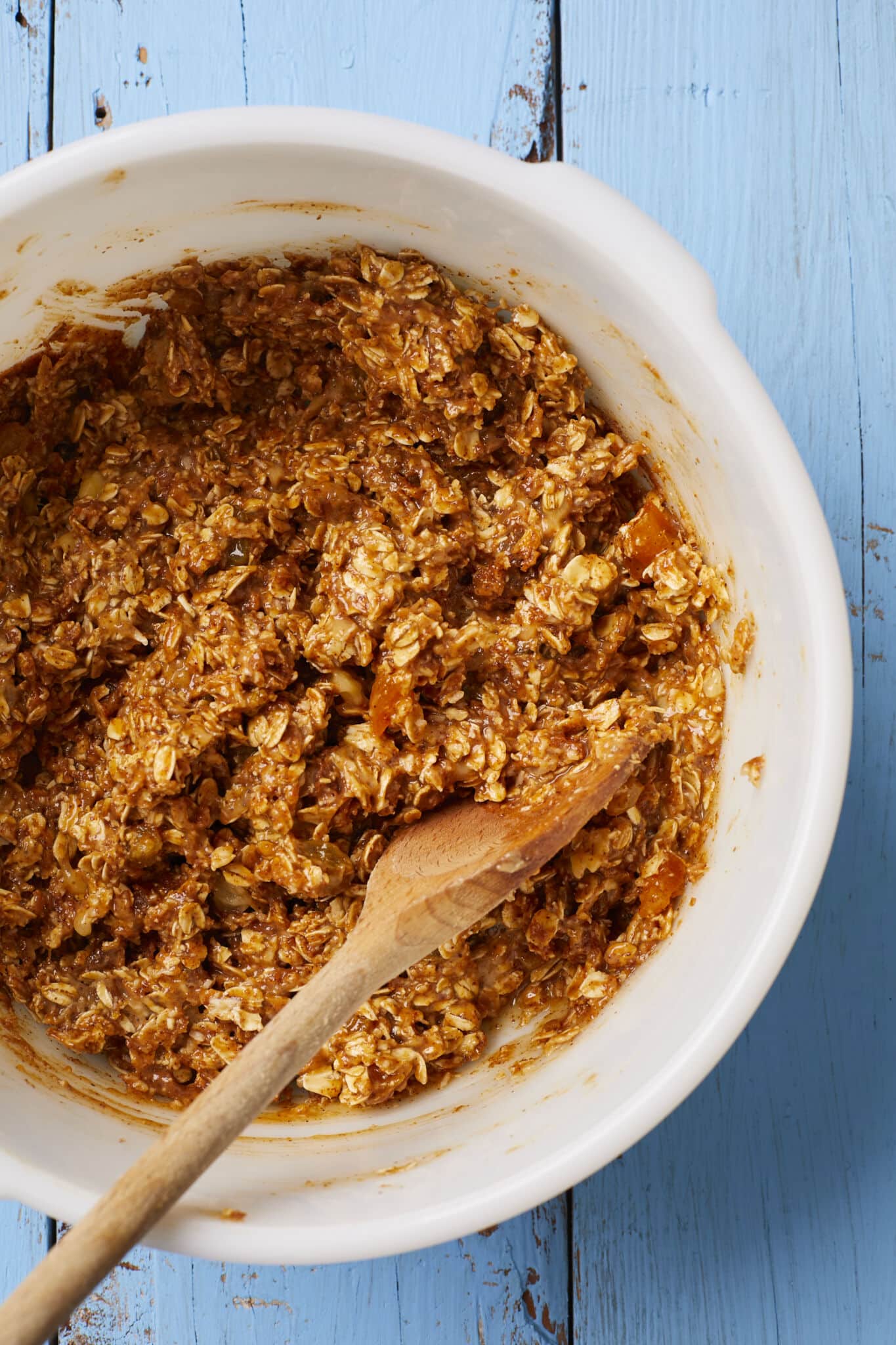 Step-by-step instructions: use a wooden spoon to mix dry ingredients including rolled oats, dried fruit, coconut flakes cinnamon, salt together then add in wet ingredients including peanut butter, mashed bananas, eggs and honey into a well-combined thick batter. 