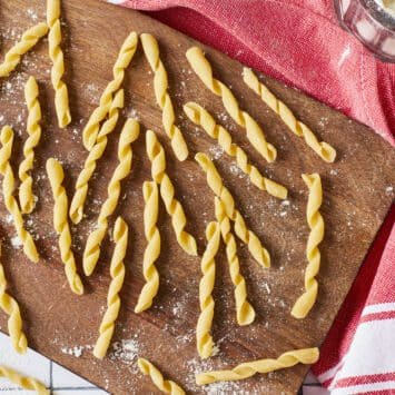Yellow semolina Busiate pasta is in characteristic cord shape and placed on a lightly floured wooden board, with a red color kitchen towel underneath.