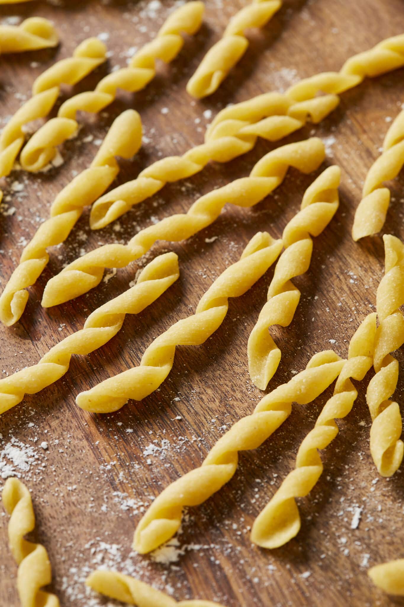 A close shot of yellow semolina Busiate pasta: Busiate is in coil or cord shape and placed on a lightly-floured wooden board. 