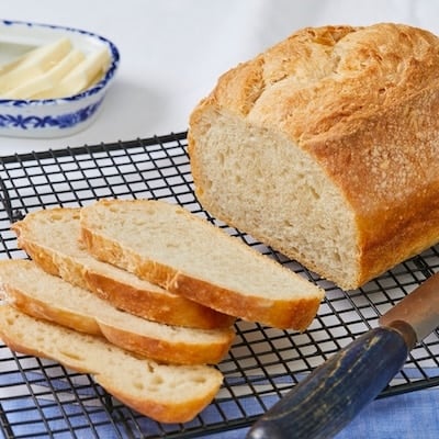 Half loaf od No Knead Sandwich Bread on the rack with four slices. Served with butter on the side.