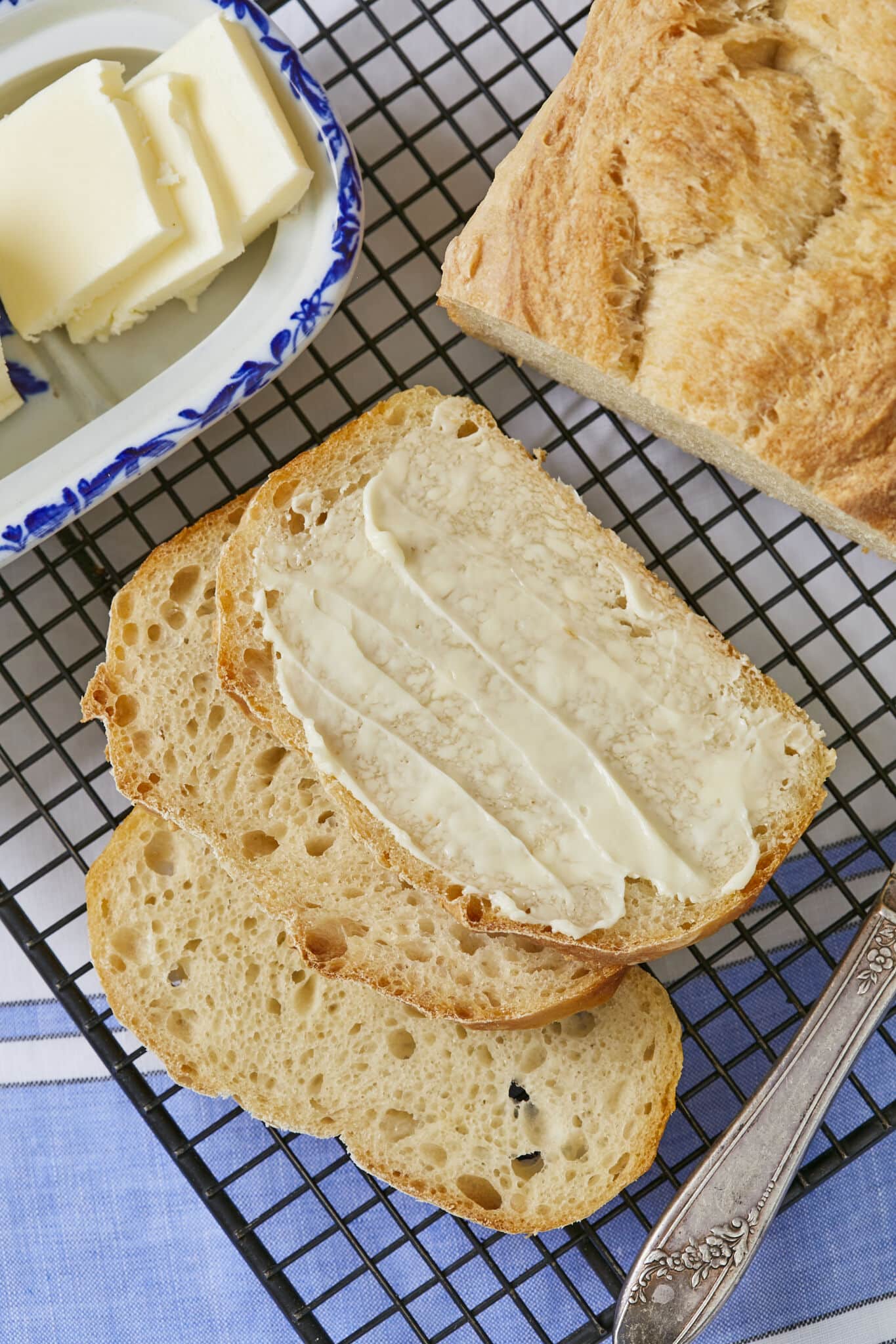 Butter is to the left of half golden sandwich loaf. Three slices are cut out and one slice has softened butter spread on top. 