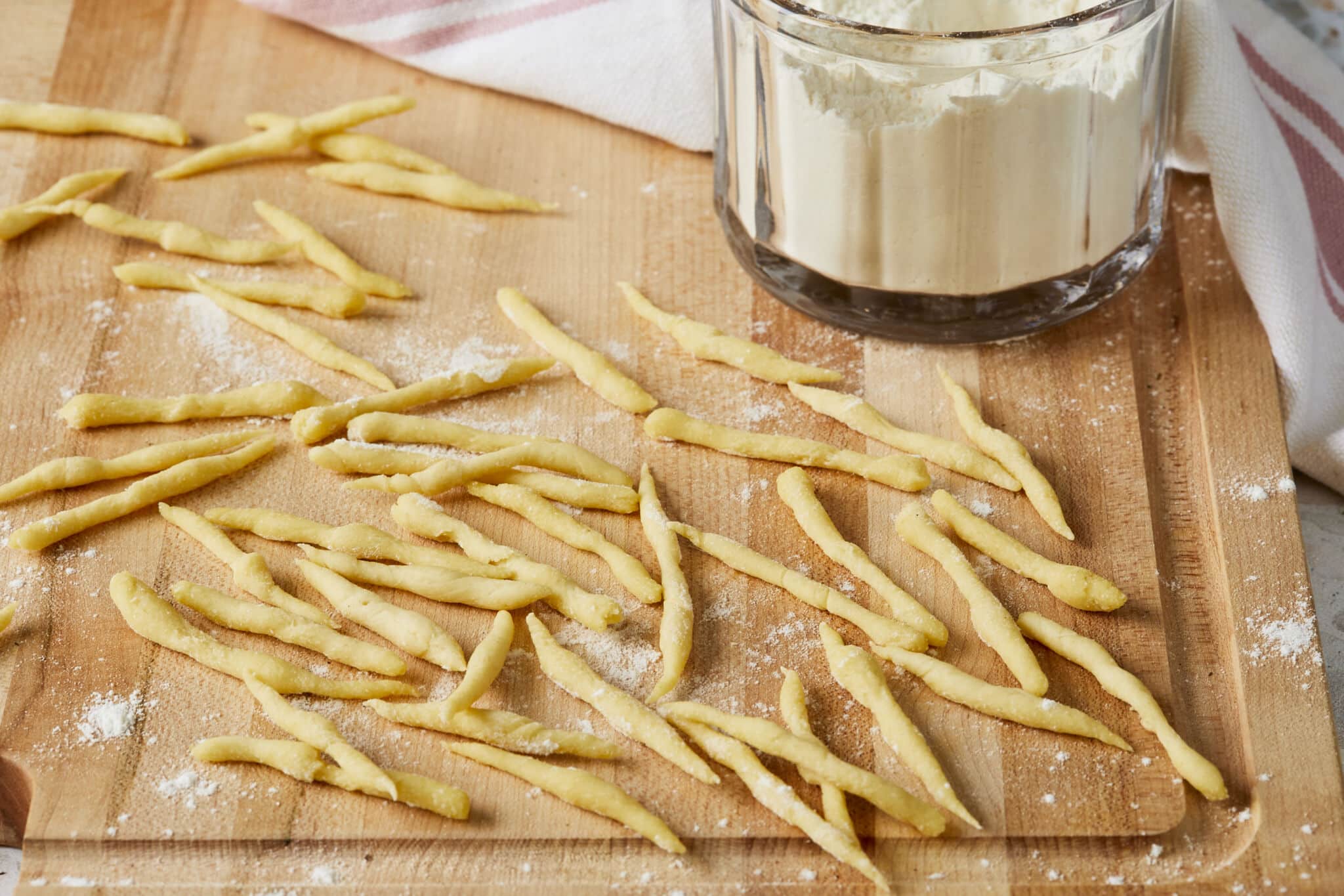Semolina Trofie pasta is placed on a lightly floured wooden board. Their notable small, short, and irregular cylinder shape contributes to Trofie clinging to and absorbing sauces effectively.