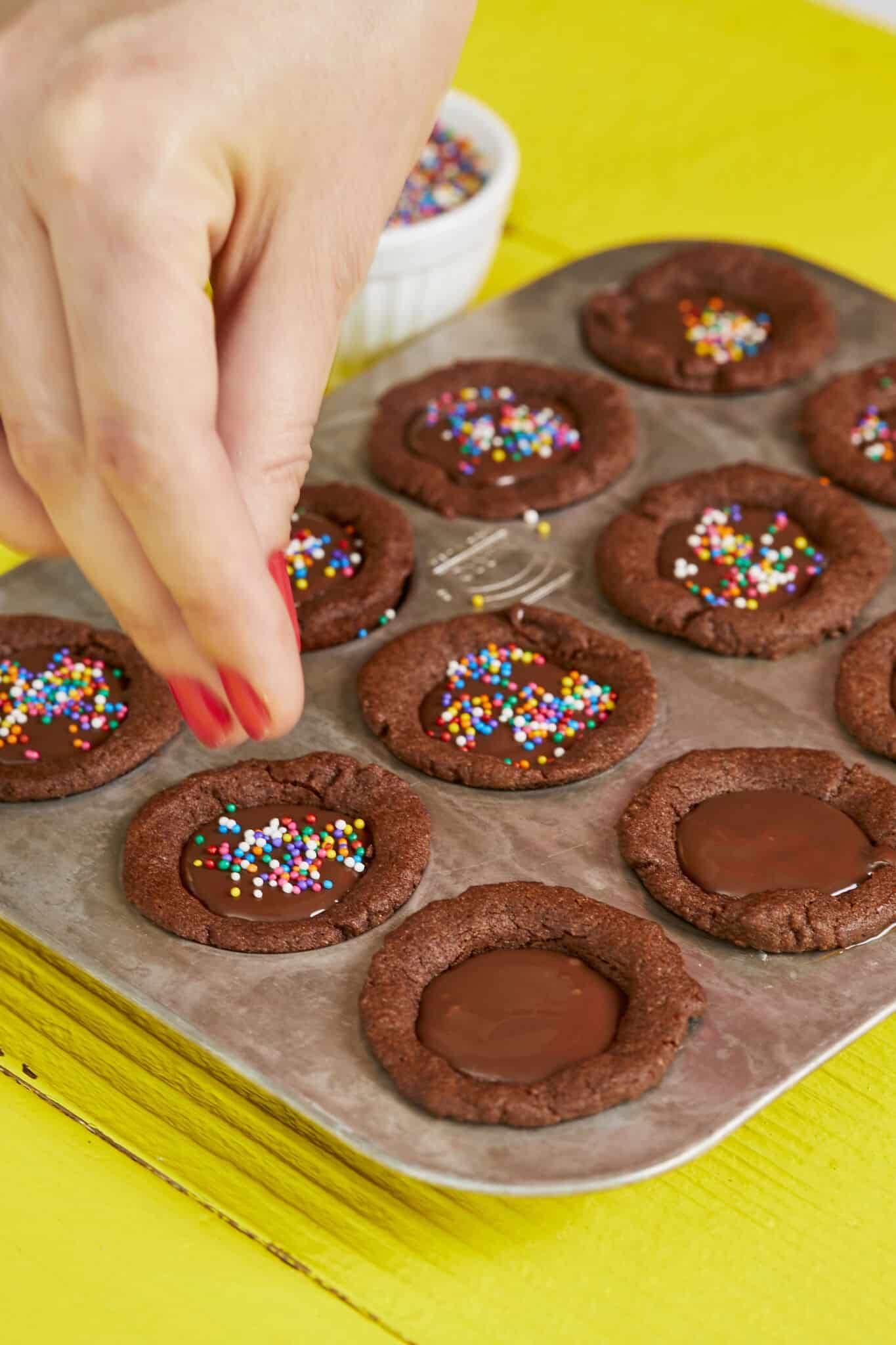 Chocolate Cookie Cups are baked and set perfectly in a 12-well mini cupcake pan. These bite-size cups have lightly crispy edges, soft and chewy inside with a silky ganache filling. They're decorated with colorful sprinkles. 