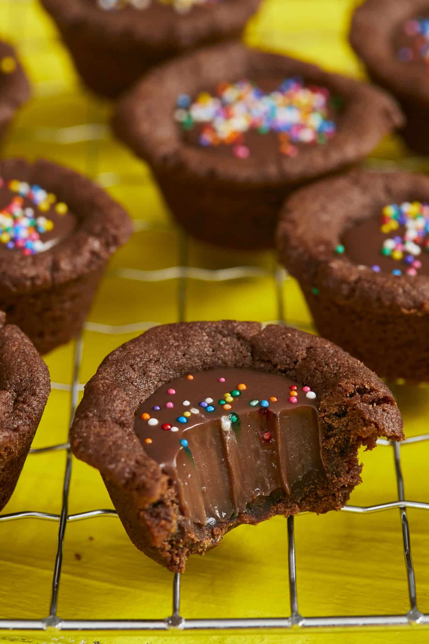 A close shot at bite-size Chocolate Cookie Cups showing that they are in signature chocolate brown color, decorated with colorful sprinkles, have lightly crispy edges, soft and chewy inside with a silky ganache filling.