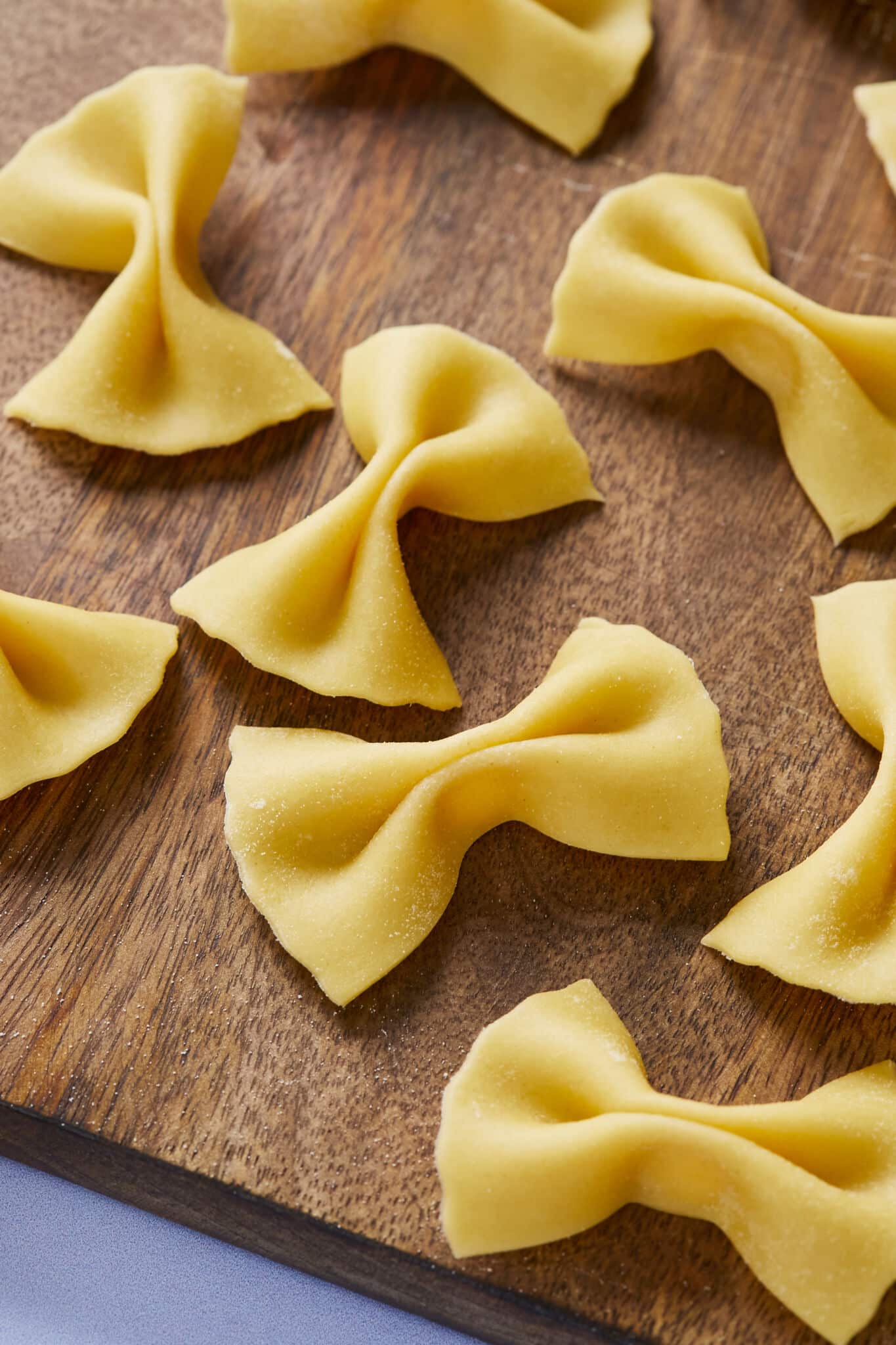 A close shot at butterfly-shaped Farfalle Pasta with perfect crevasses and fluted edges drying on a wooden board. 