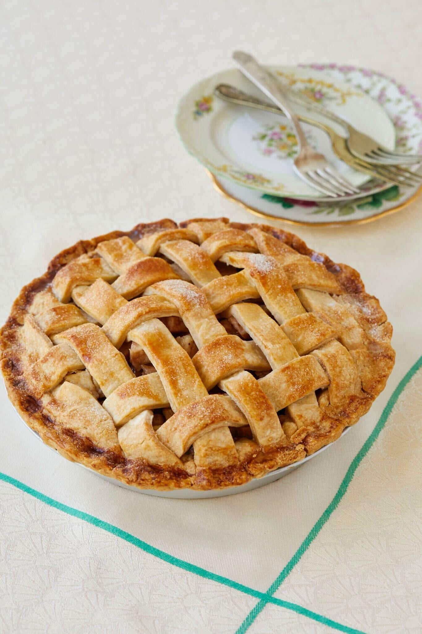 The Flaky and Easy Pear Pie is baked perfectly golden brown all round the edges and the lacie topping. Two floral dessert plates and three forks are on the side. 