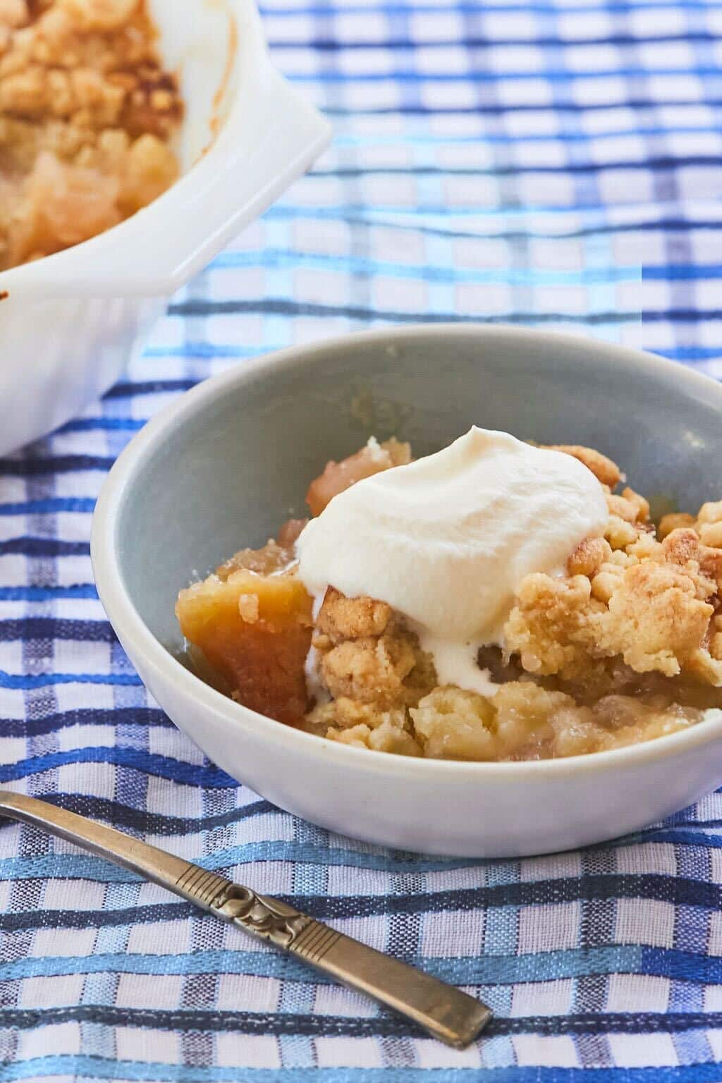 Authentic Irish Apple crumble is served in a bowl next to the baking dish. It's loaded with soft sweet apples, golden crispy crumble and topped with freshly whipped cream.