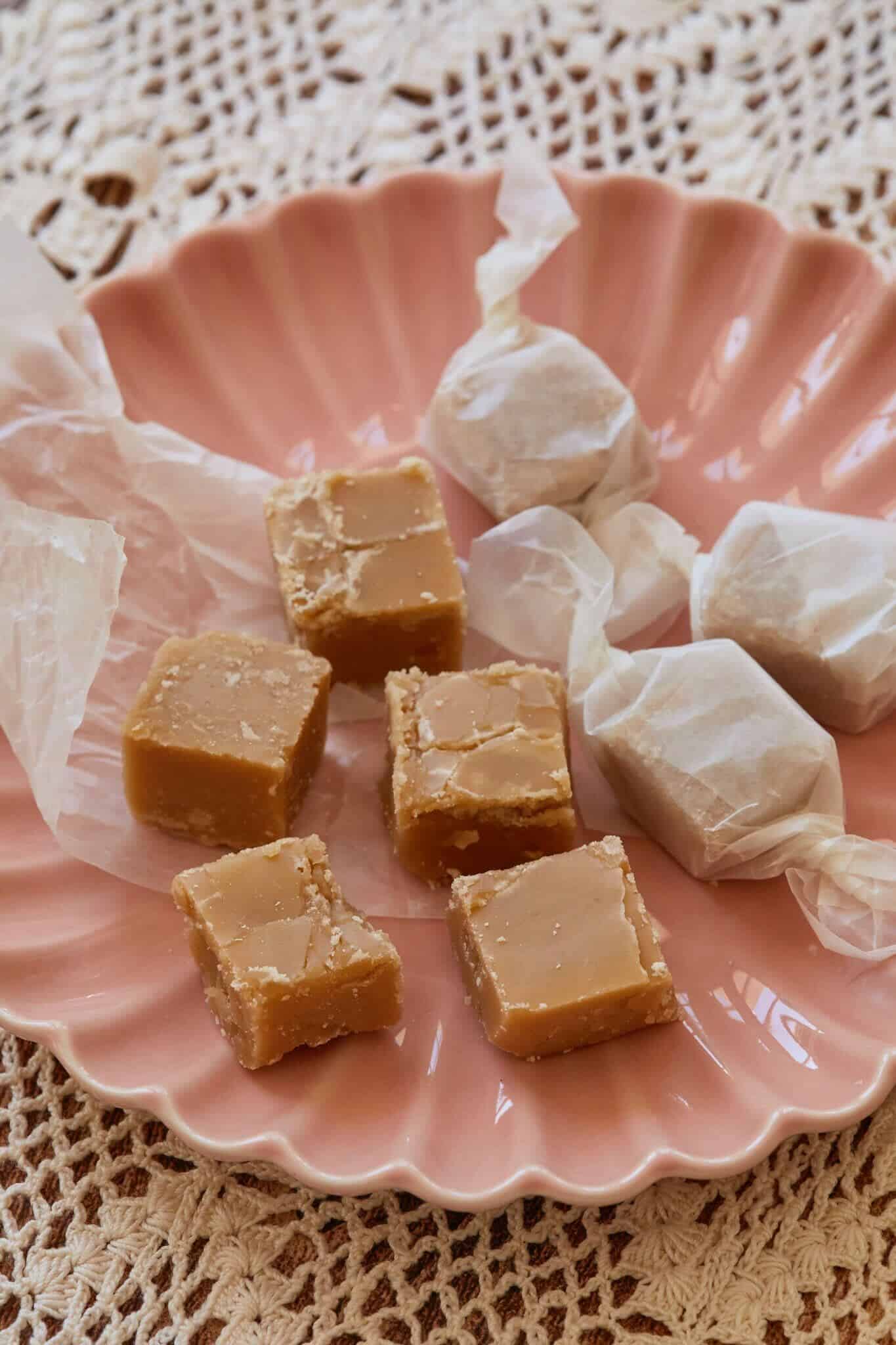 Square homemade candy made with maple syrup are served on a pink dish. The homemade candy has a slightly gritty texture from the sugar crystals and is wrapped in parchment paper. Using only 3 ingredients makes it the magic of Fall Recipes.