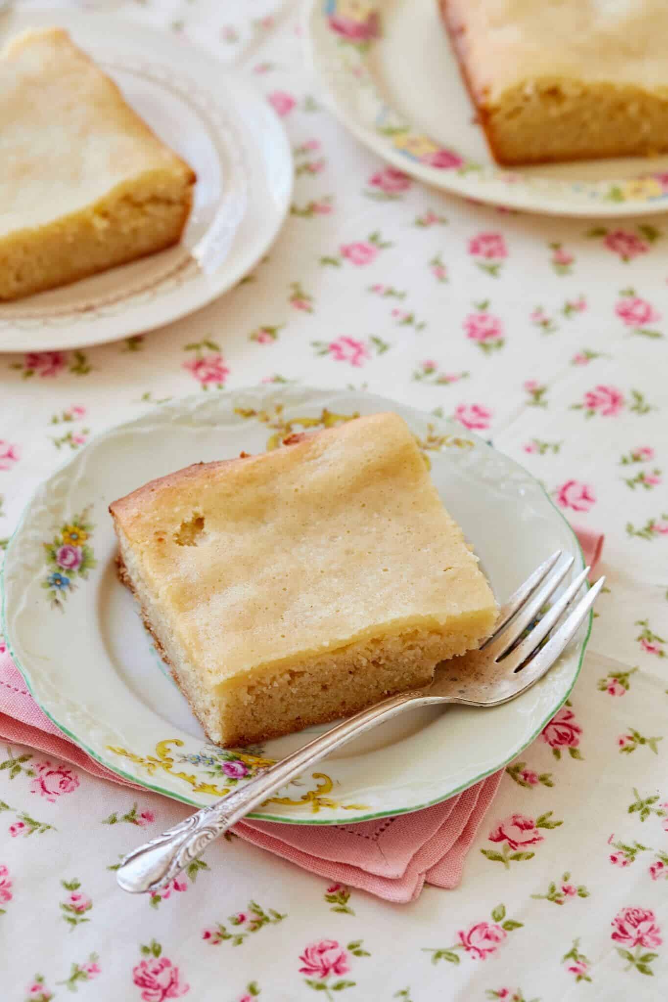3 slices of Maple Gooey Butter cake are served on dessert plates. The cake looks moist and soft on the inside with a smooth top on the outside and with golden and slightly crispy edges. 