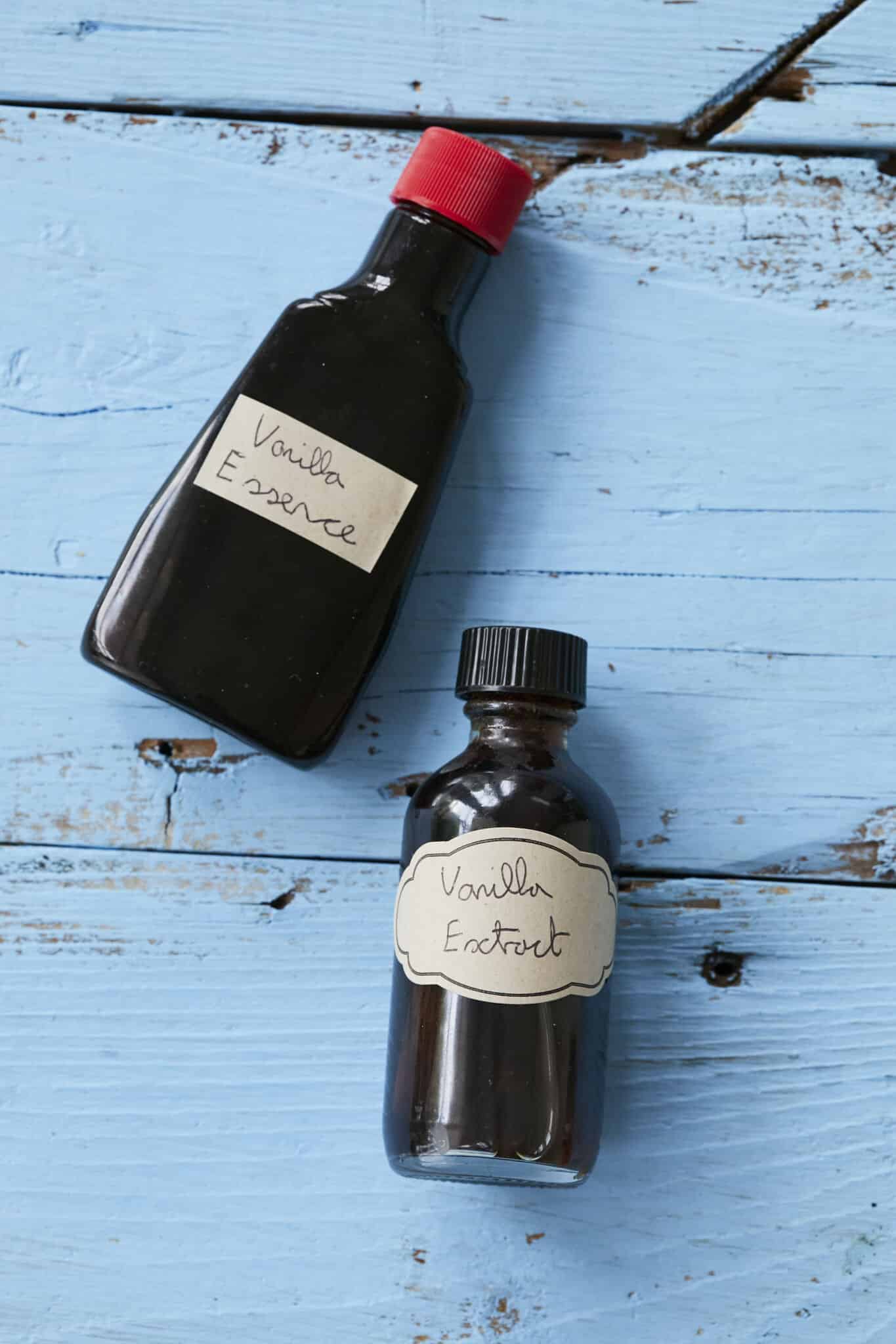 A bottle of Vanilla Essence with a red cap is next to a bottle of Vanilla Extract with a black cap for comparison. 