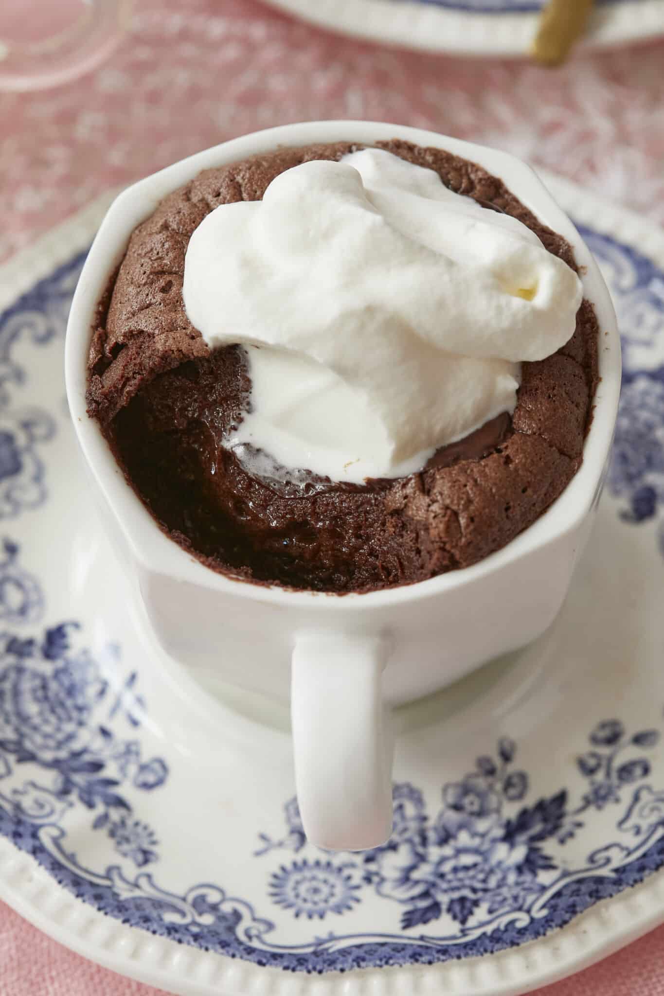 A close shot at baked hot chocolate that has one bite taken shows the gooey center and lightly crispy edge. It's paired with softly whipped cream.