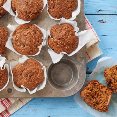 Healthy Bran Muffins are baked perfectly in liners in the muffin tin. They look moist, soft and packed with raisins. A Healthy Bran Muffin is cut in half, one half is topped with butte, the other half shows the soft, moist and fluffy inside packed with raisins.