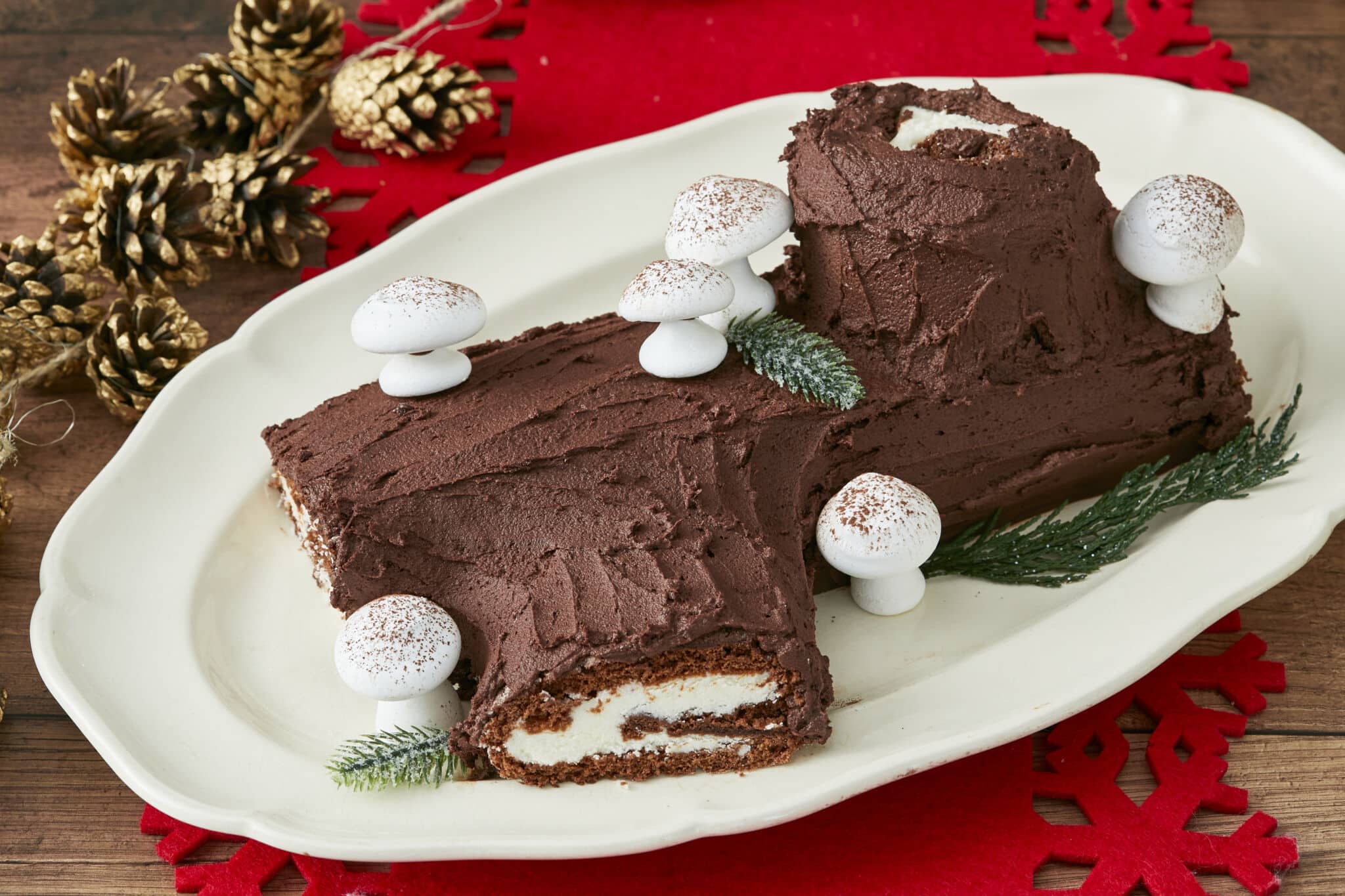 Christmas Yule Log (Bûche de Noël) is served on a big white platter. It's a chocolate sponge cake roll filled with vanilla buttercream, frosted with chocolate buttercream, and decorated with meringue mushrooms to look like a rustic yule log.