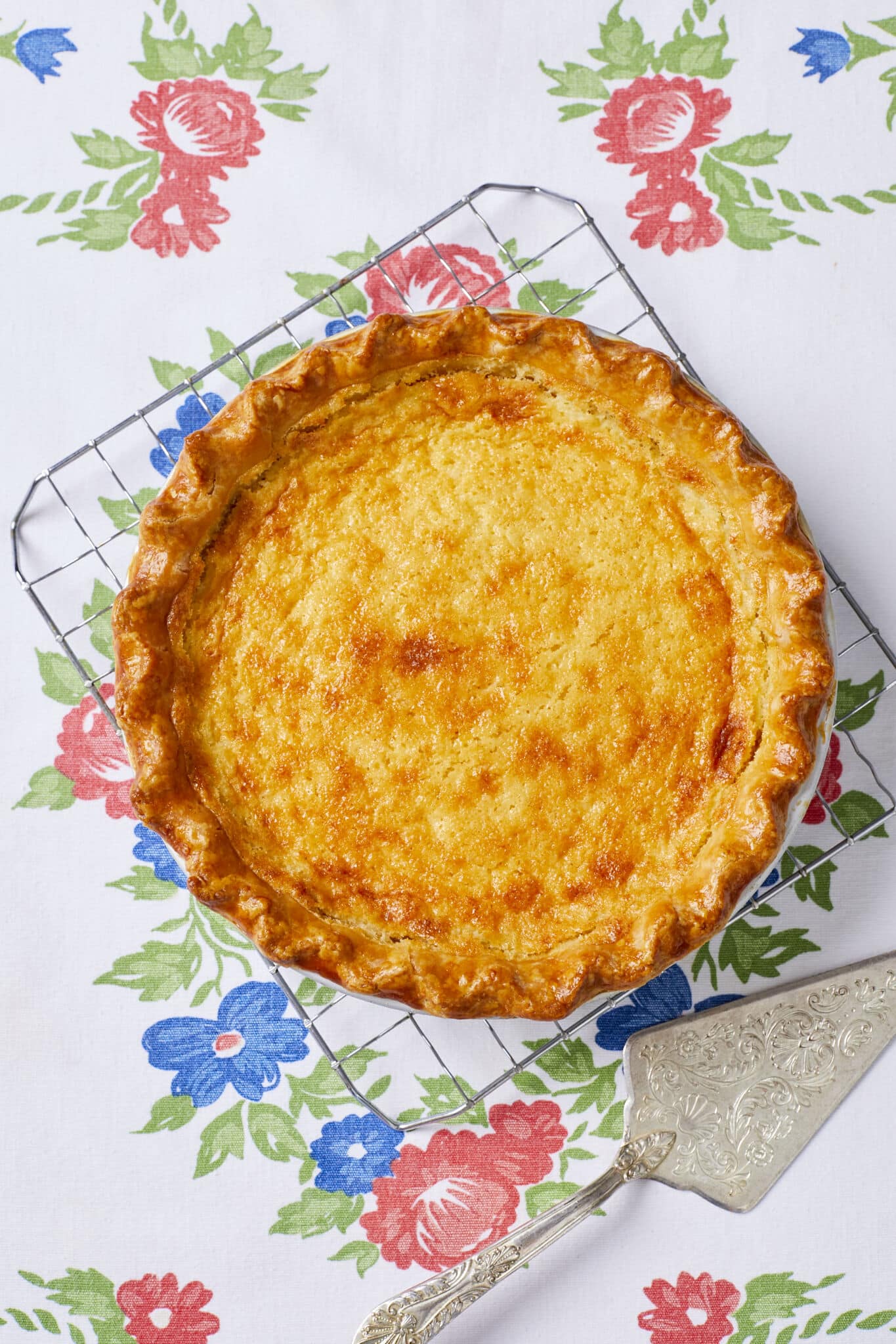 An Irresistible Buttermilk Pie is baked perfect with golden-brown crust and creamy, tangy filling. It's cooling on a wire rack. 