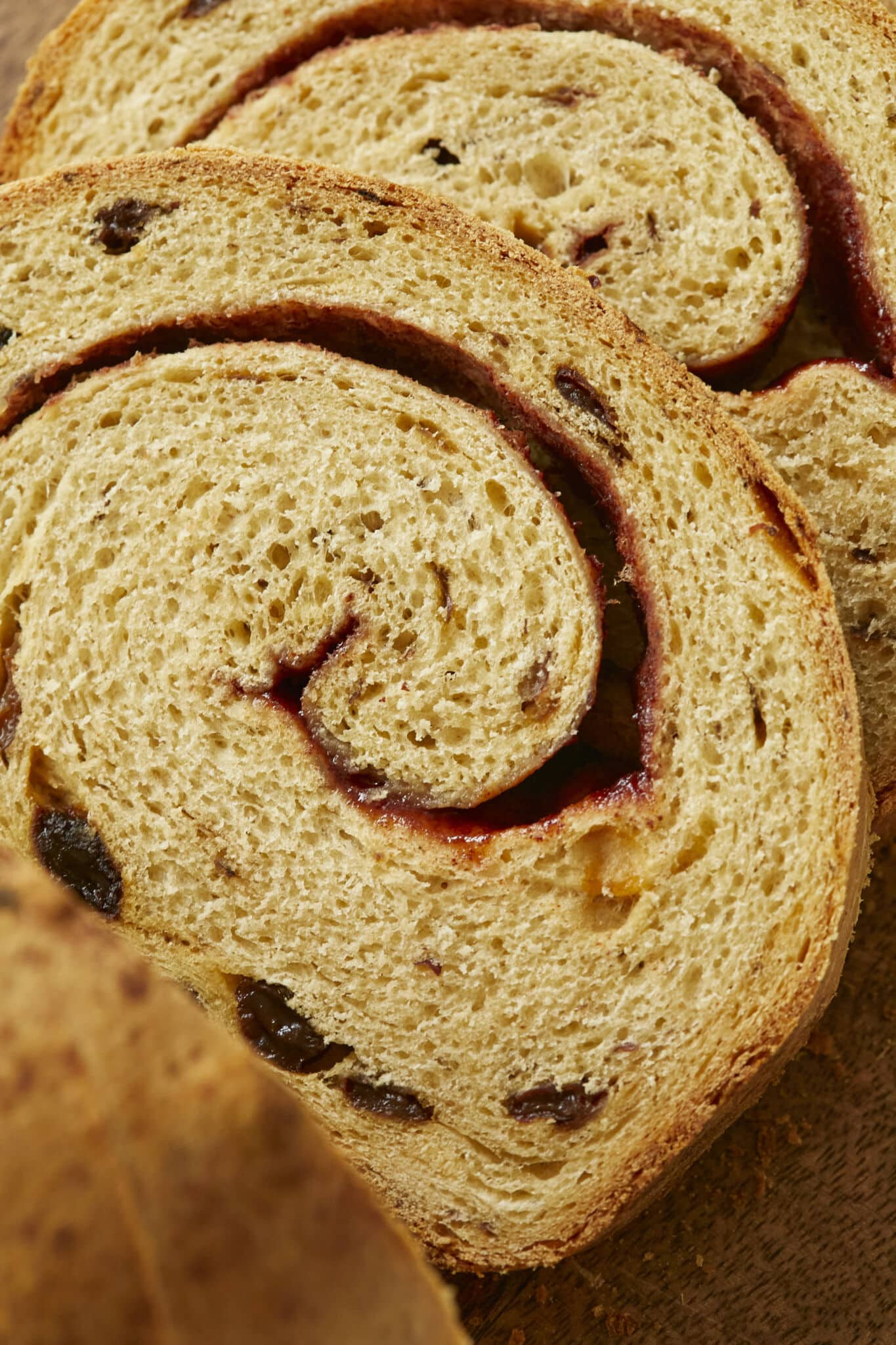 A close-up shot at the sliced Cinnamon Swirl Raisin Bread shows its golden-brown and slightly crispy crust, tender and even crumb, scattered raisins, and cinnamon swirls throughout upon slicing.
