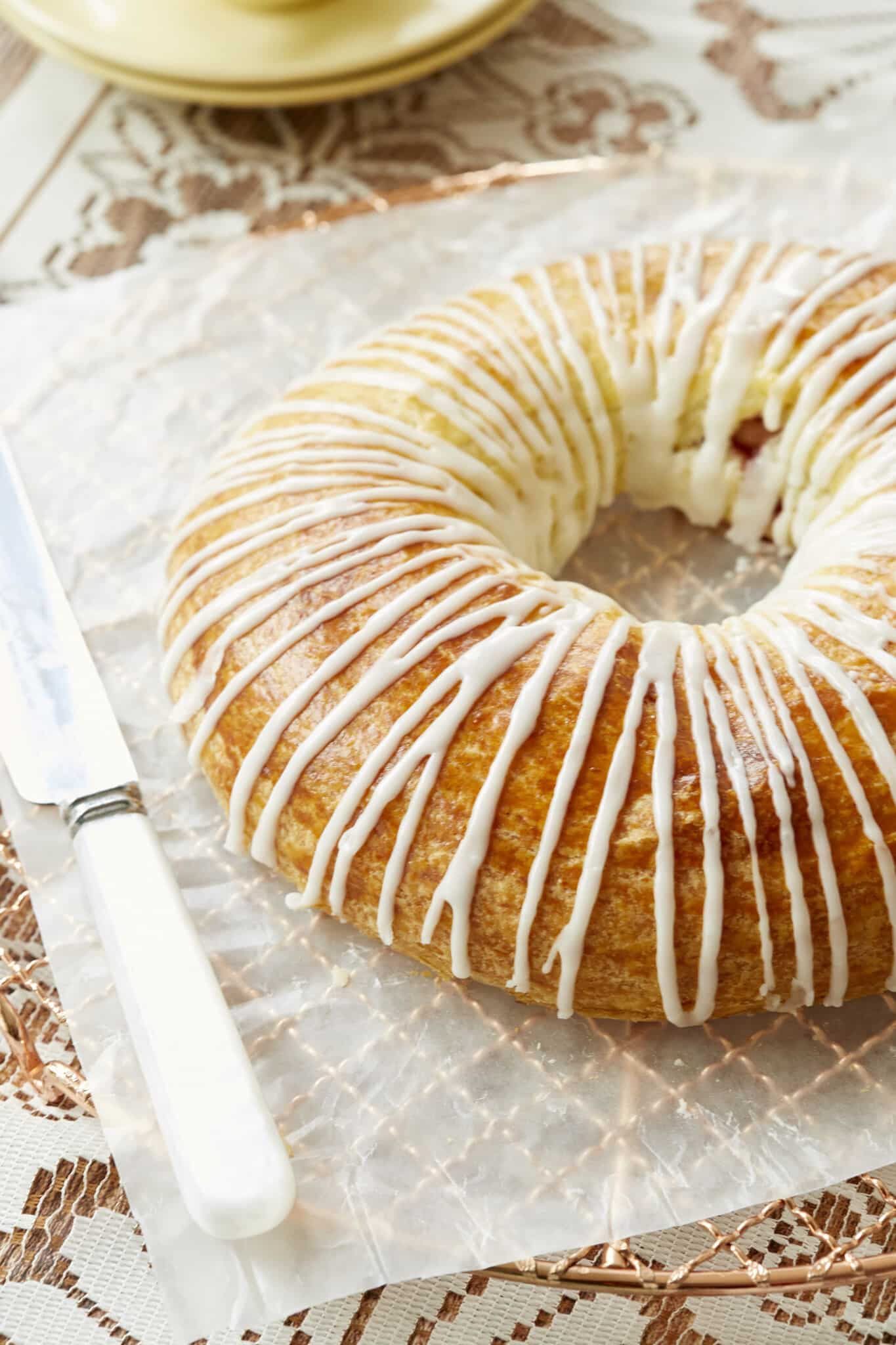 A close shot at a gorgeous Danish Kringle shows it golden brown top gleaming with zig zags of creamy icing. 