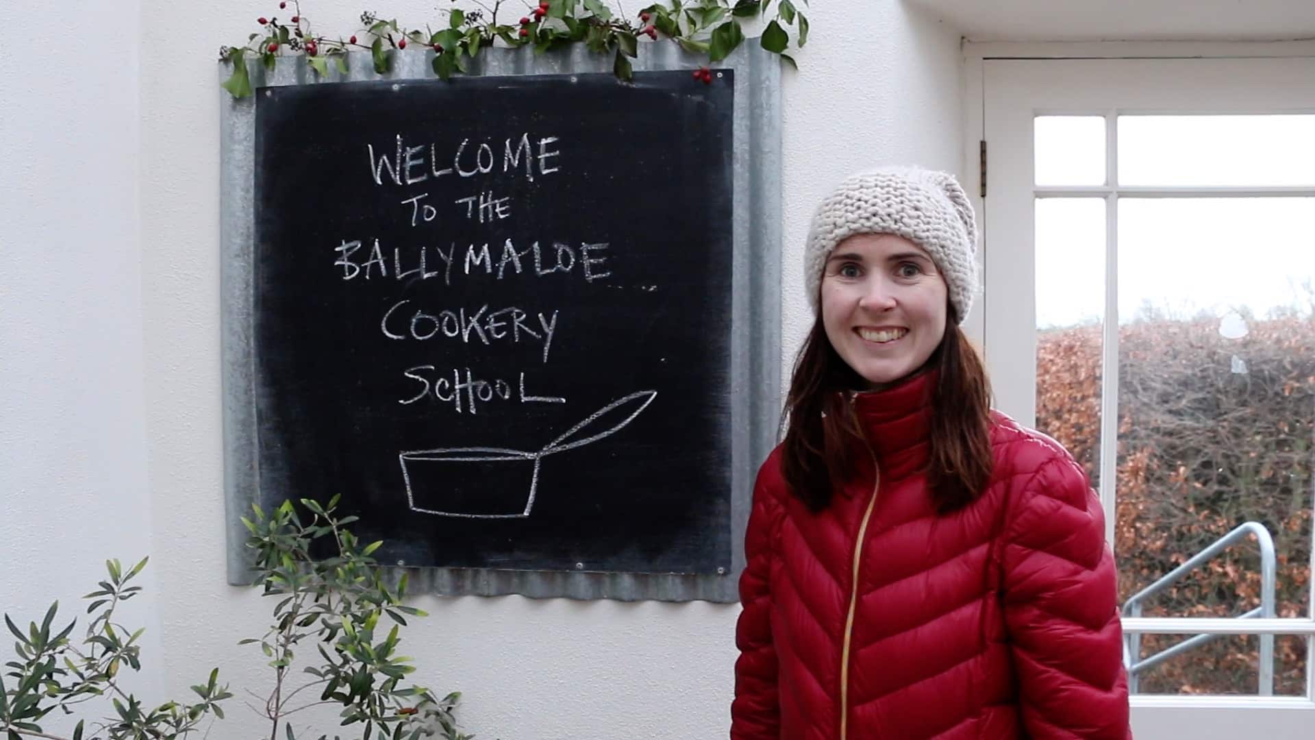 Gemma Stafford is in red, standing next to the "Welcome to the Ballymaloe Cookery School" sign. 
