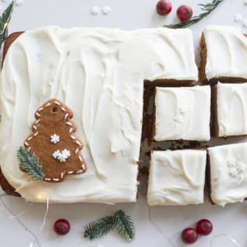 A Perfectly-Spiced Gingerbread Sheet Cake is cut into generous squares and ready for serving. The cake is moist and soft, topped with velvety cream cheese frosting. A star-shape gingerbread cookie and a Christmas tree shape gingerbread cookies are served together.