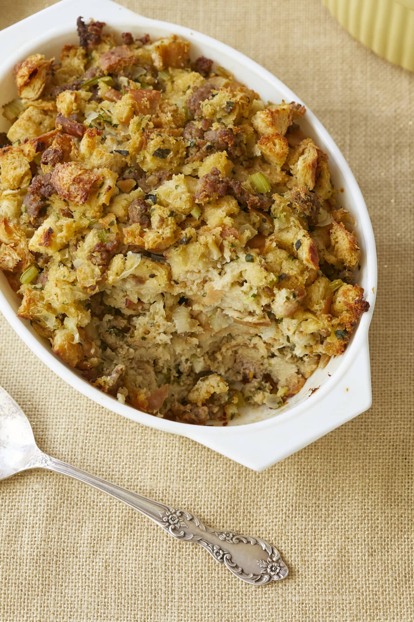 Classic Sage Sausage Stuffing is baked in a white milk galss baking dish. Toasted white bread is tossed with savory sausage, earthy sage, and aromatic onion and celery, mixed with in eggs and broth to a fluffy, moist casserole with tempting craggy browned bits!