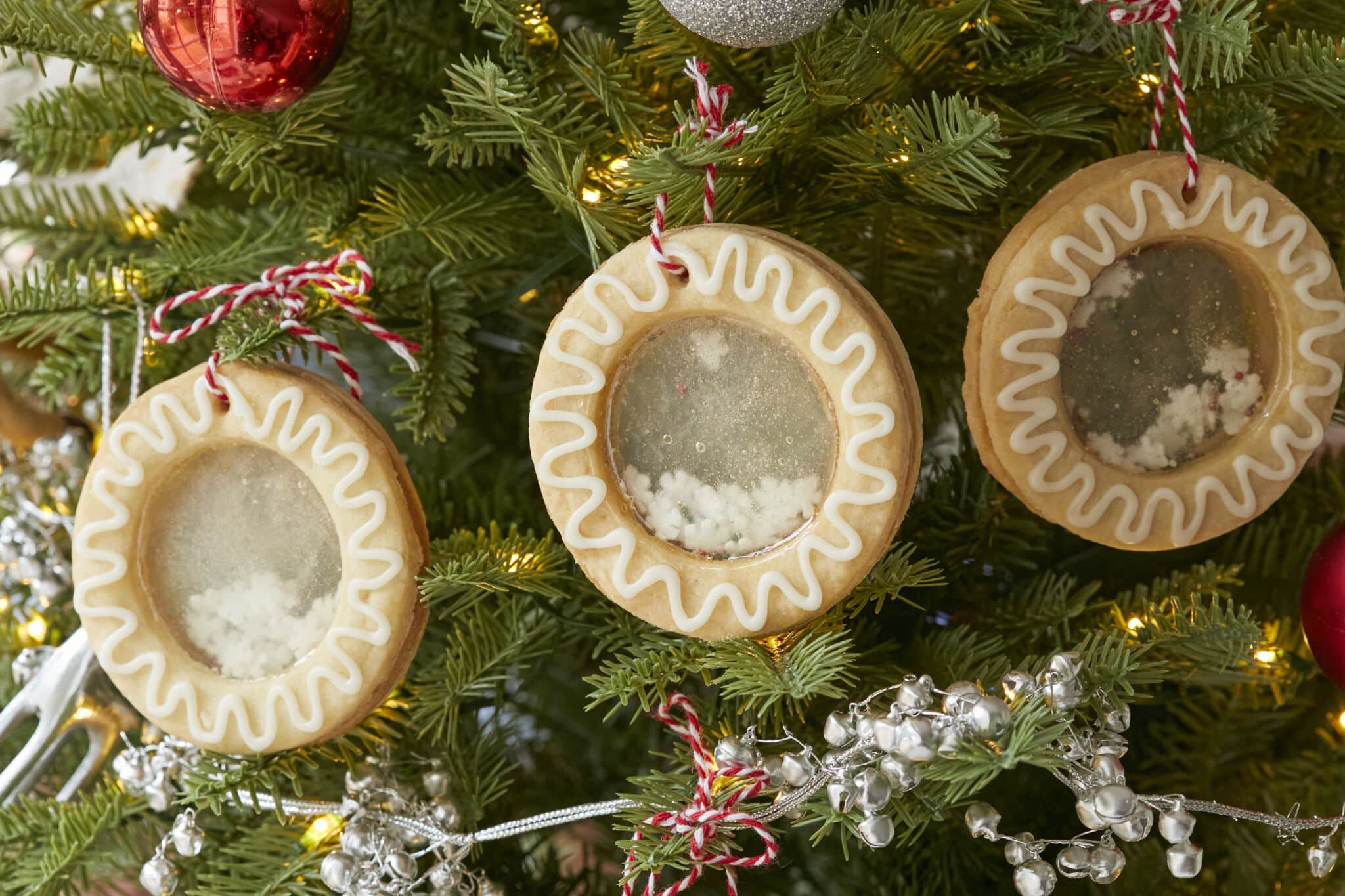 Three Snow Globe Cookies are hanging in the Christmas tree. They are made with crispy traditional Irish shortbread, which are creatively dressed up with snow-white icing. The clever filling formed a shiny mirror center, casting a glow throughout the joyful space. 