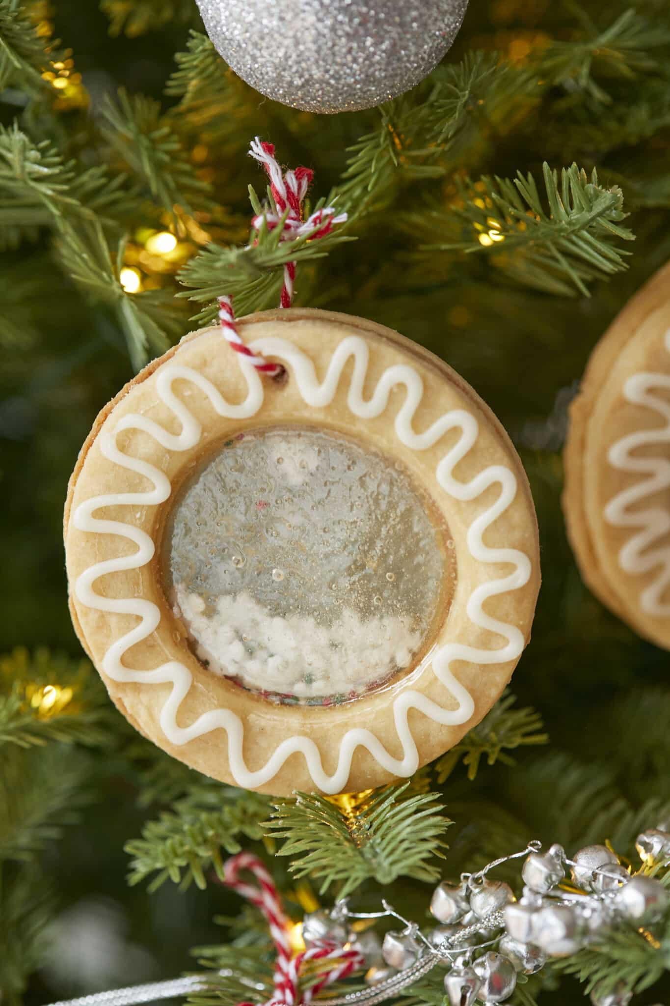 Snow Globe Cookies are hanging in the Christmas tree. They are made with crispy traditional Irish shortbread, which are creatively dressed up with snow-white icing. The clever filling formed a shiny mirror center, casting a glow throughout the joyful space. 