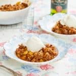 Boozy Whisky Apple Crisp is baked in a milkgalss Pyrex baking dish with sweet, buttery baked apples covered with a cinnamon oatmeal-cinnamon crispy top. Two servings are ready in dessert plates with ice cream on top.