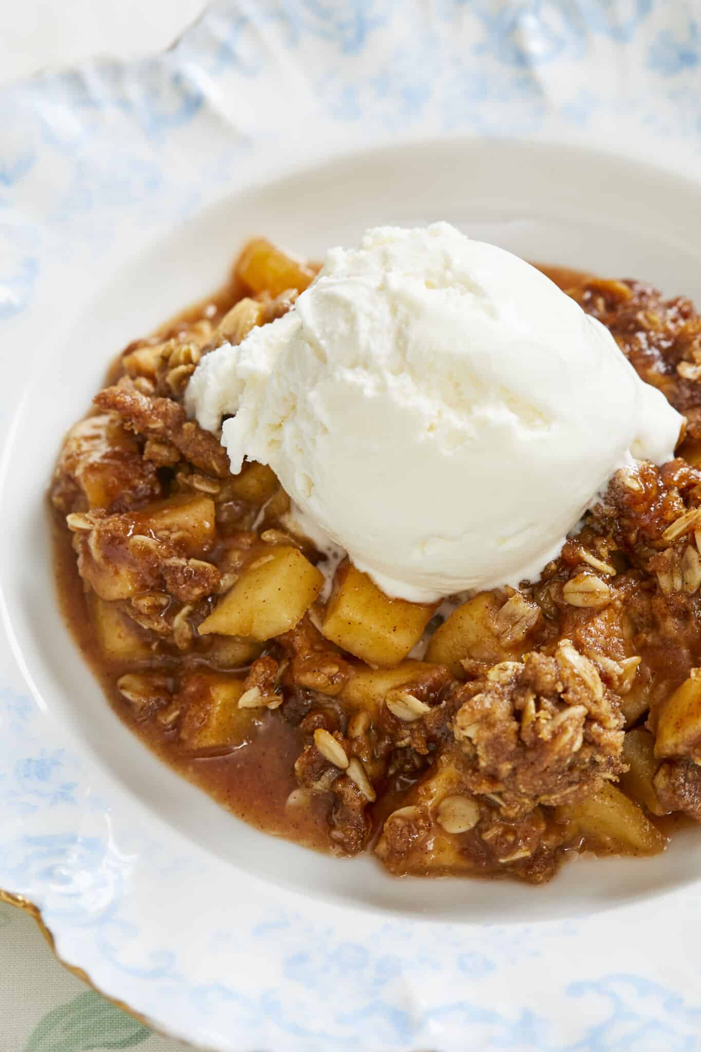 A close-up shot at Boozy Whisky Apple Crisp in a blue floral dessert plate with ice cream on top. 