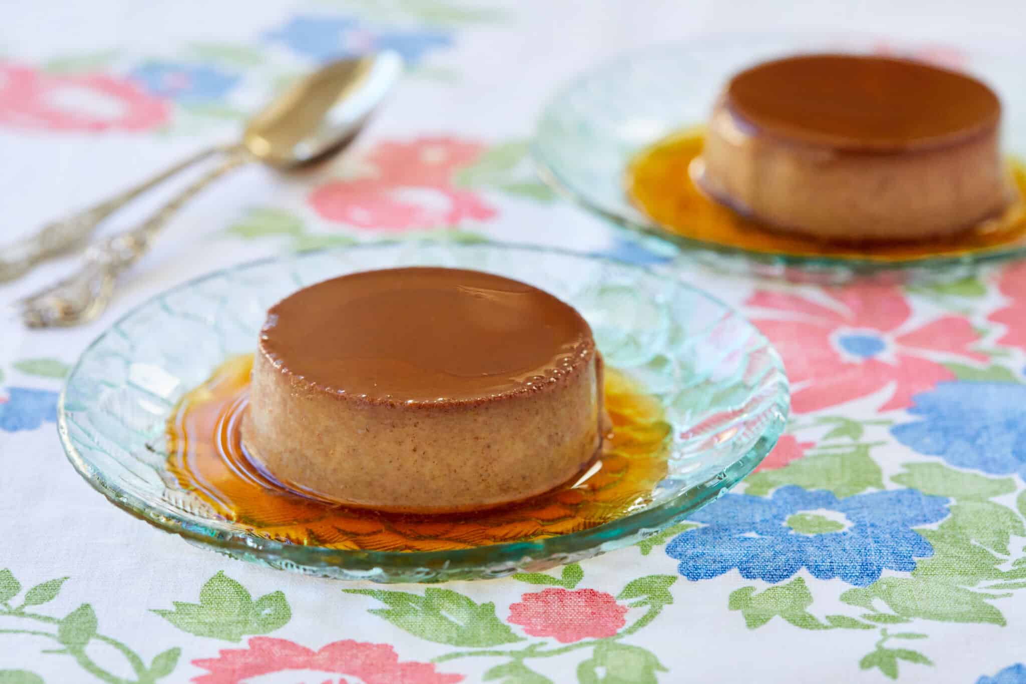 Two servings of chocolate Crème Caramel are served on glass dessert plates, with silky and tender custard topped with decadent sweet caramel.