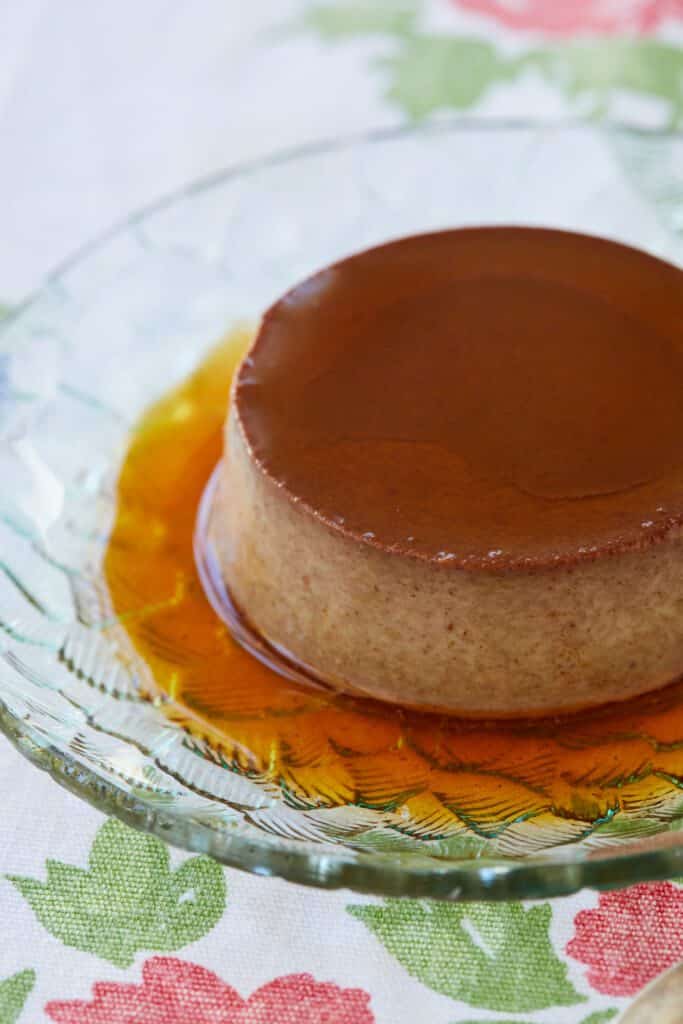 A close-up shot a chocolate Crème Caramel served on a glass dessert plate, shows its silky and tender custard topped with decadent sweet caramel.