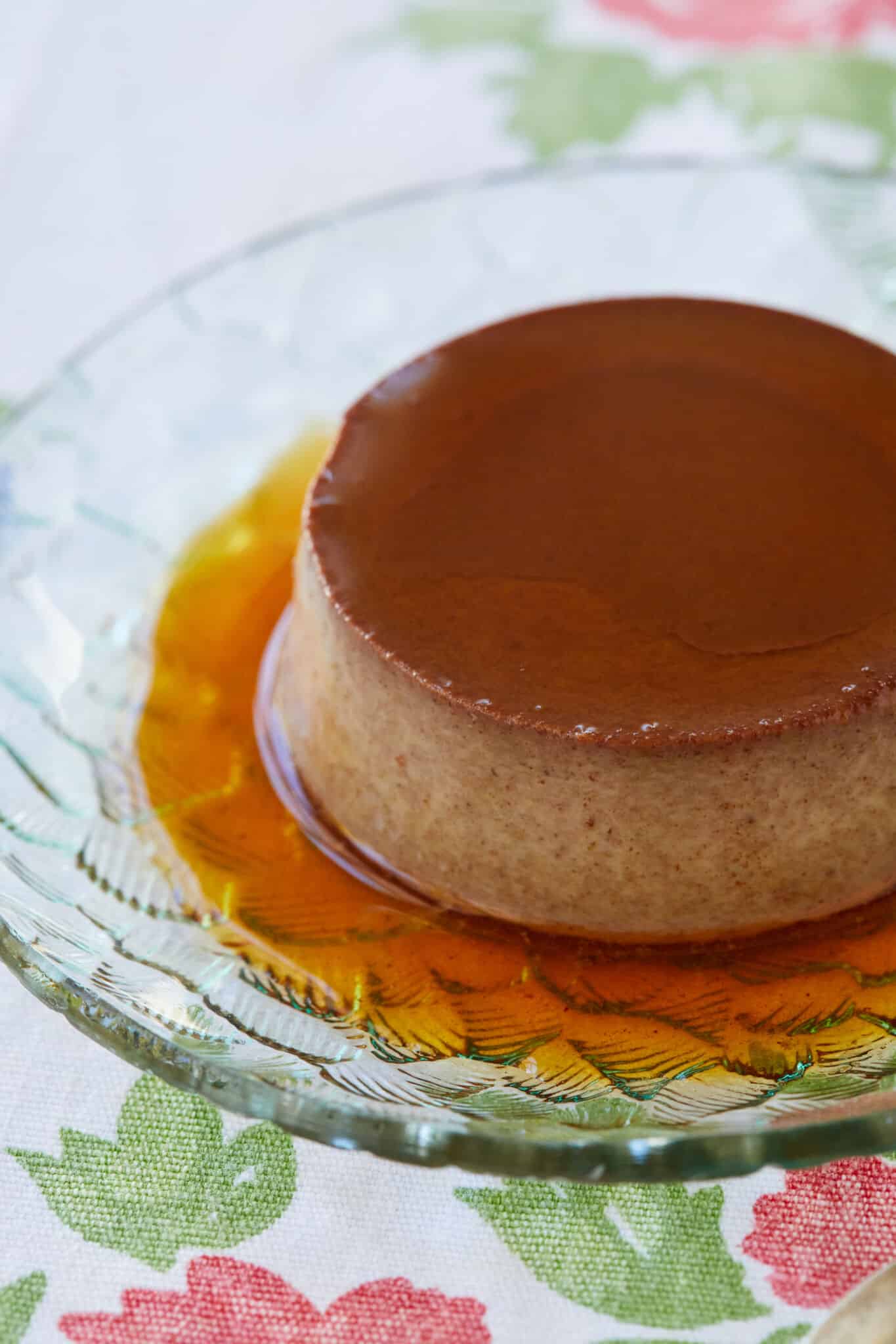 A close-up shot at the chocolate Crème Caramel served on a glass dessert plate, with silky and tender custard topped with decadent sweet caramel. 