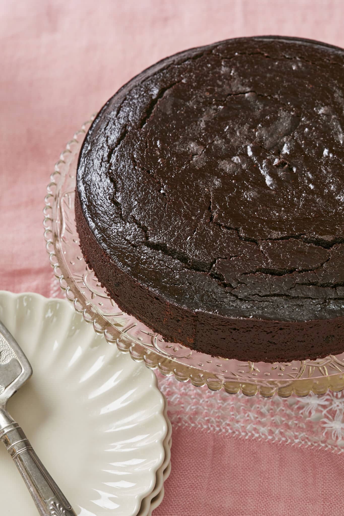 A rich, moist decadent Irish whiskey Chocolate Cake is served on a glass cake stand. The top is shiny and slightly crinkled. 