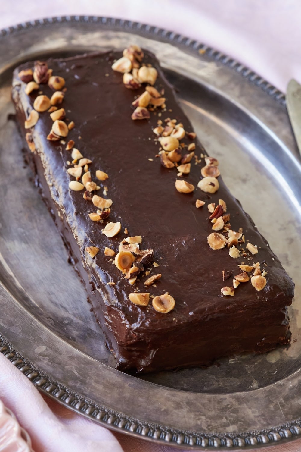 A loaf of Marjolaine Cake with chocolate ganache topping and hazelnuts. 
