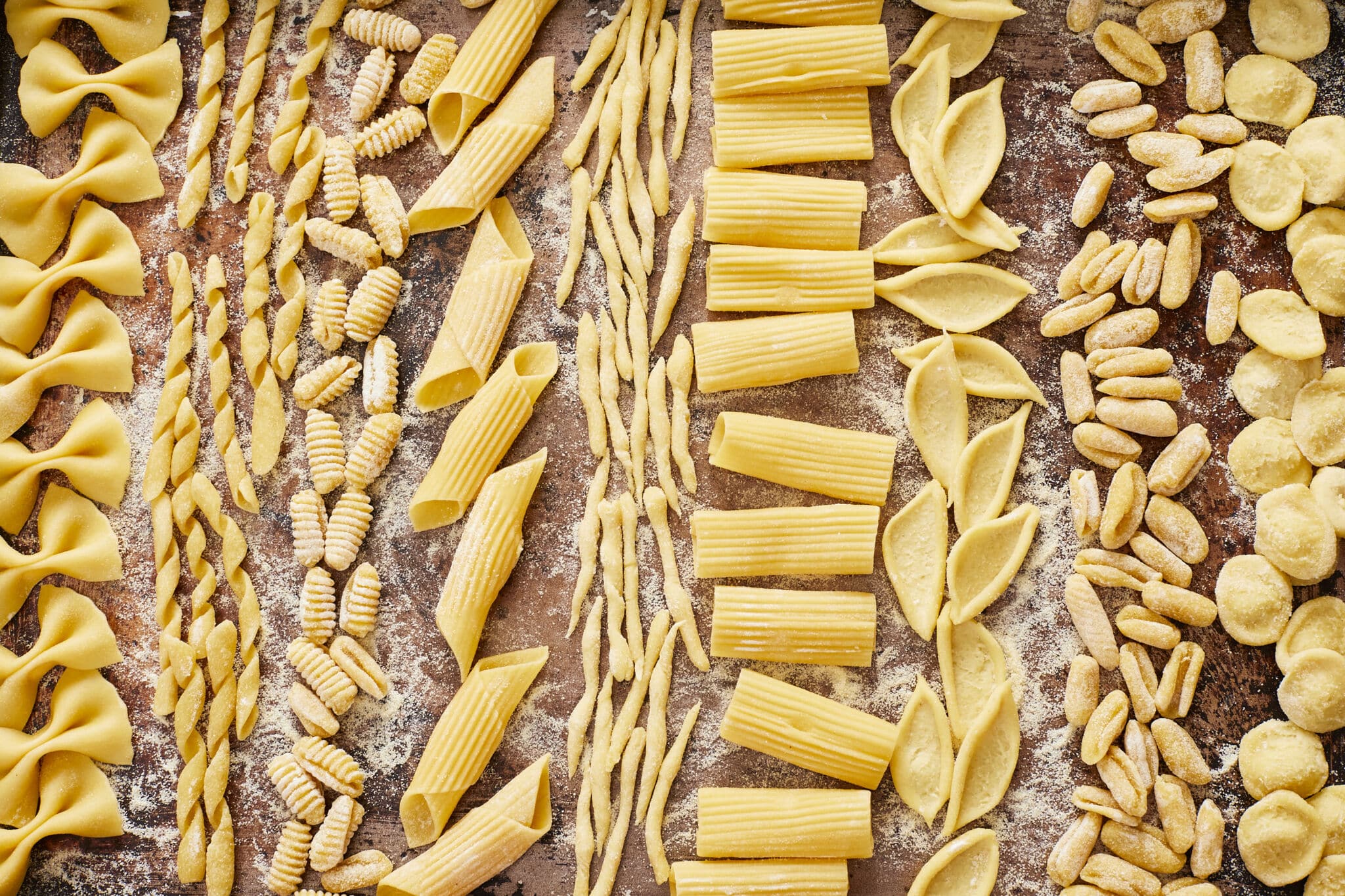 2-Ingredient Semolina Pasta is made into 9 pasta shapes, drying on a lightly floured surface. Farfalle (bow ties), Busiate (spiral), Gnocchetti (ridged small elongated shell), Penne (smooth tubes), Trofie (twisted pasta), Rigatoni (ribbed tubes), Foglie (olive leaf), Cavatelli (mini hot dog bun), and Orecchiette (small ears).