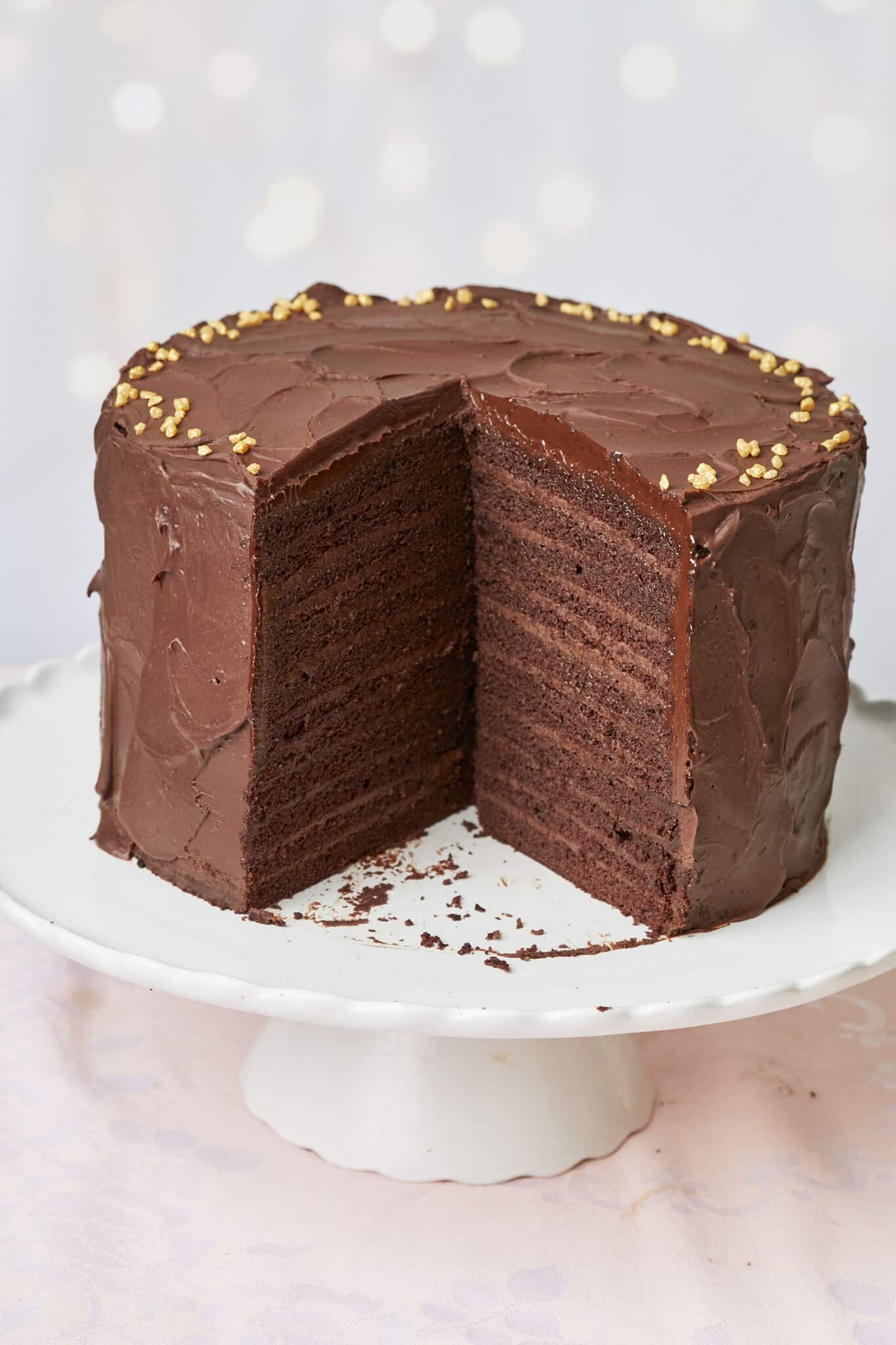 A generous slice of the 24-Layer Chocolate Cake has been cut off from the whole cake. A close-up shot shows its moist and soft crumb and silky smooth ganache on the outside and decadent chocolate pastry cream between the layers. 