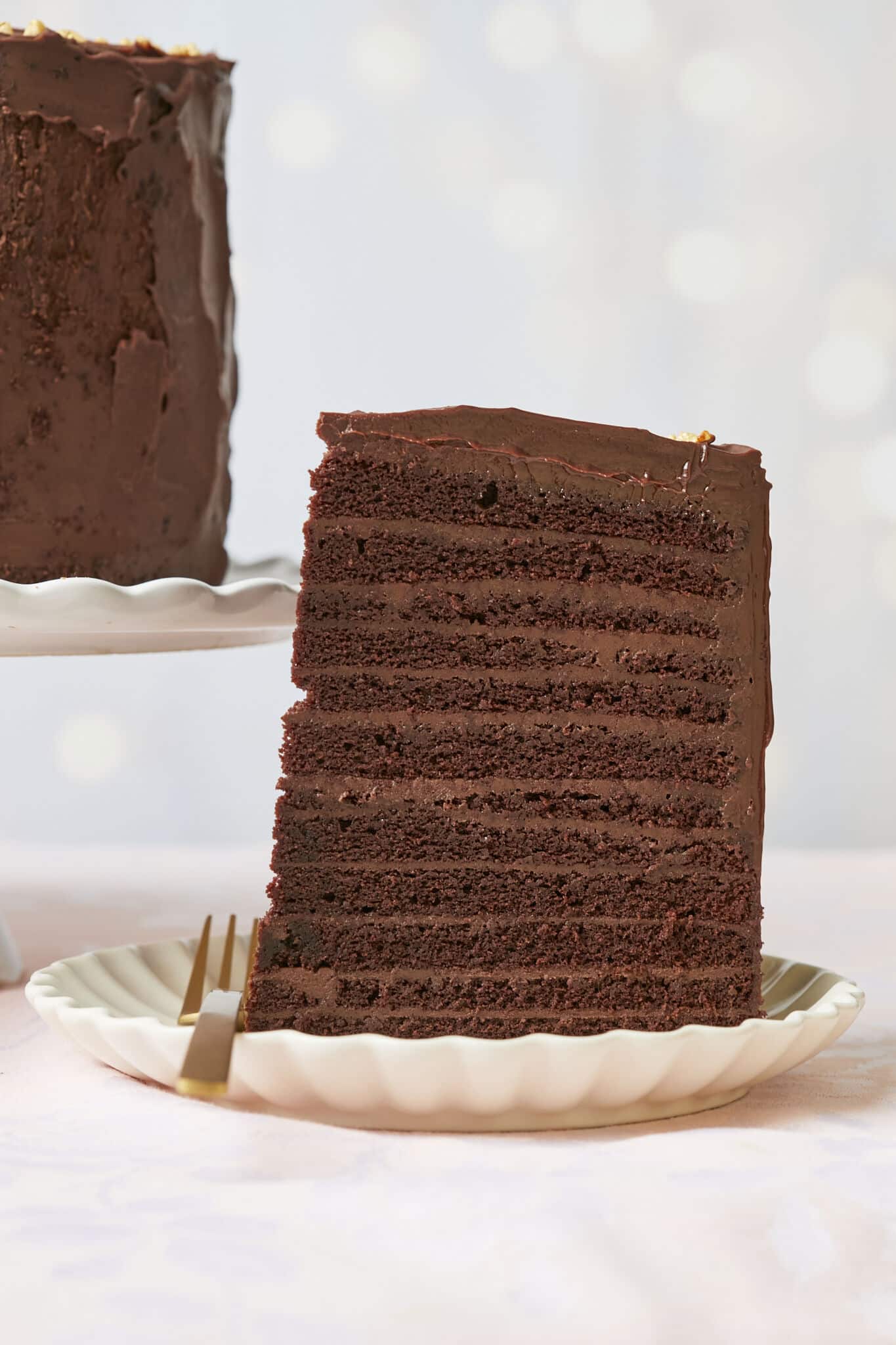 A generous slice of the 24-Layer Chocolate Cake is served in a dessert plate. A close-up shot at the slice shows its moist and soft crumb and silky smooth ganache on the outside and decadent chocolate pastry cream between the layers. 
