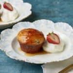 Two soft, delicate Baba au Rhum (Classic Rum Baba) cakes are served with fresh strawberry and whipped cream. Syrup is drizzled from top to bottom.